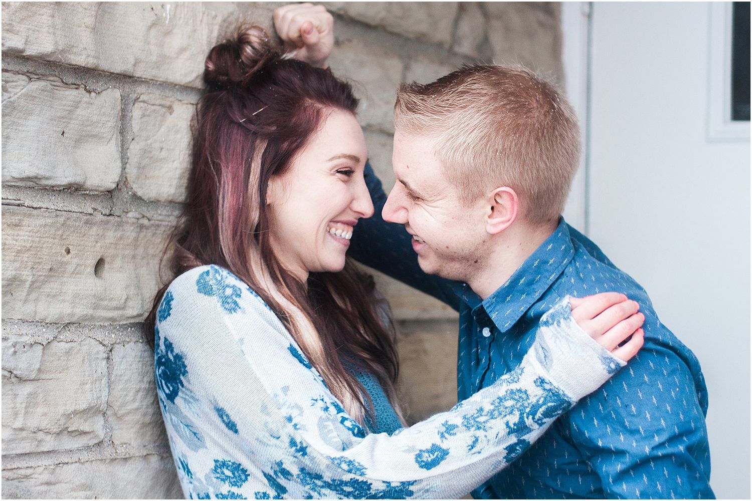 An intimate moment between a couple is captured against a rustic stone wall backdrop.