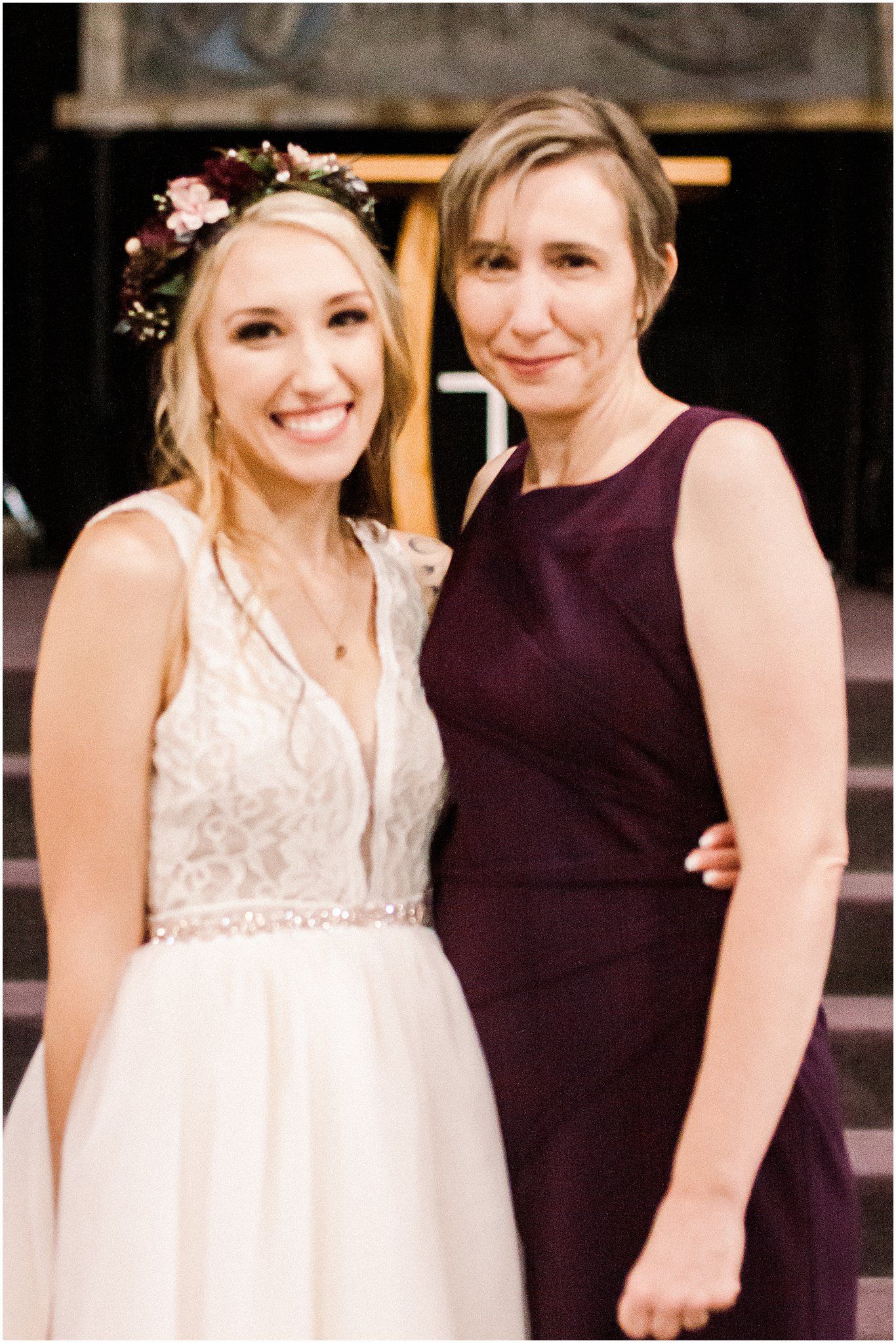 Two wedding attendees pose together against dark wooden background.
