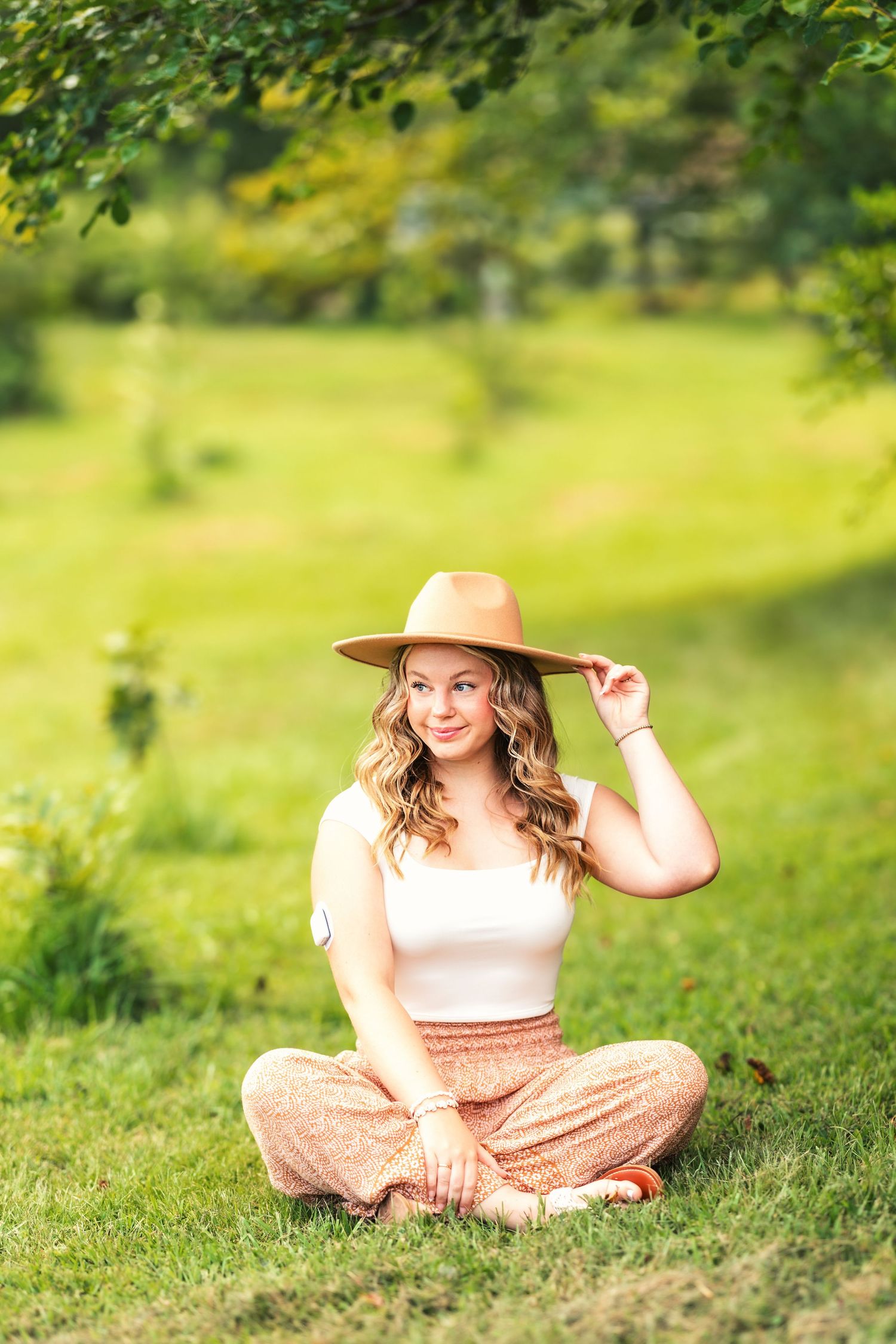 A bohemian summer look with wide-brim hat and flowing pants in a garden setting.