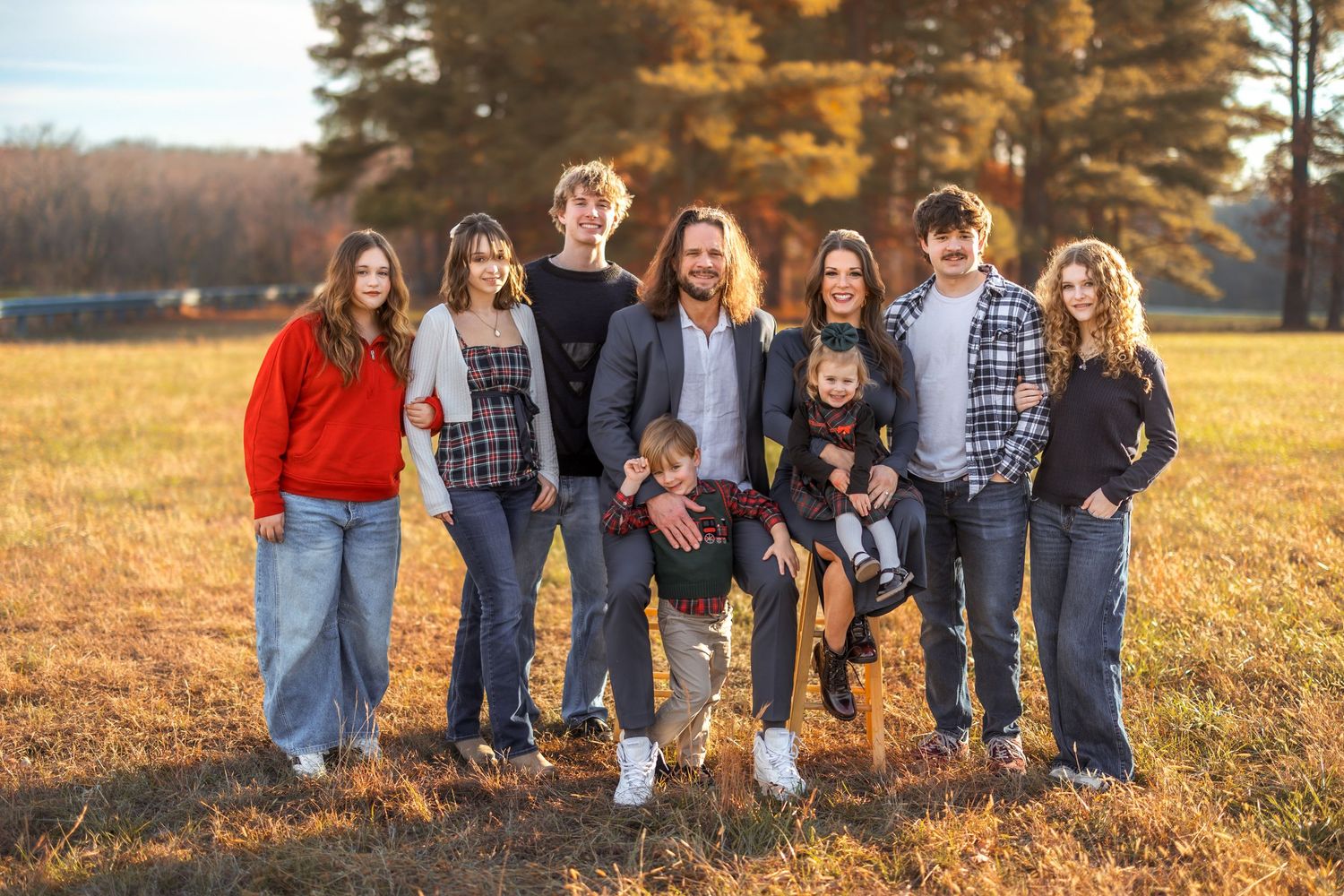 Family group poses together on a golden autumn hillside during sunset.