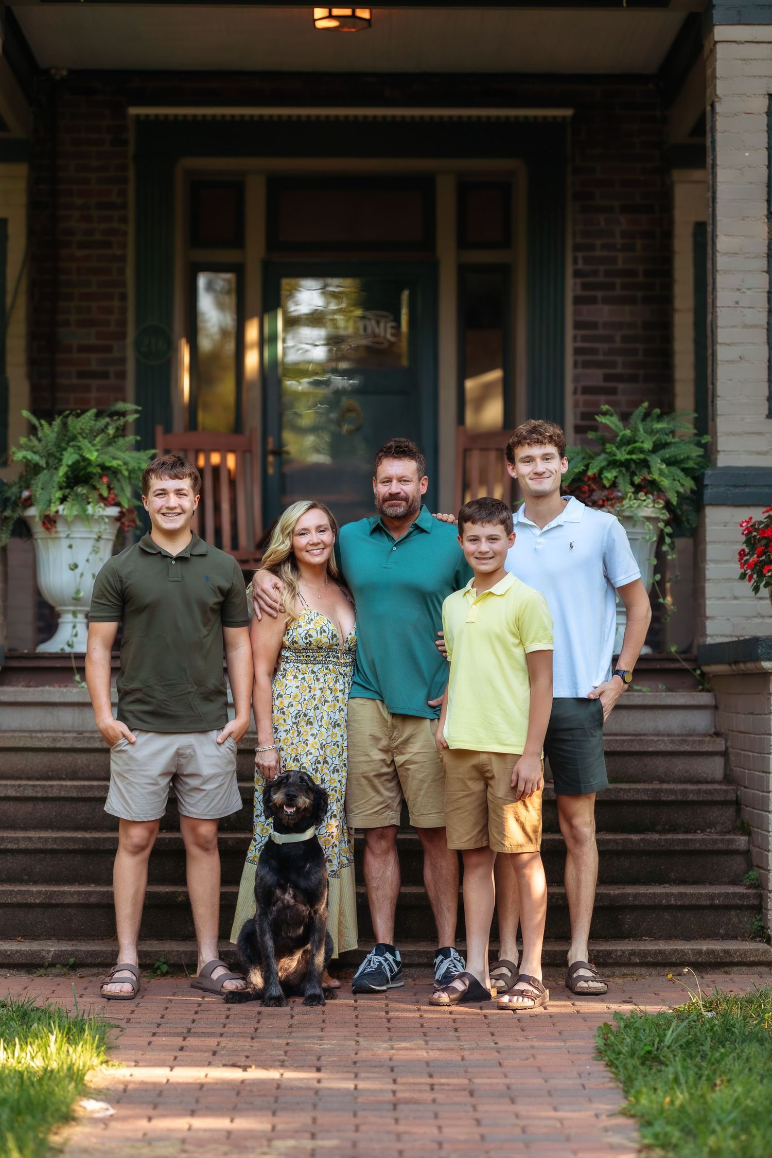 Family and their black dog gather on brick steps of a front porch for a group photo.