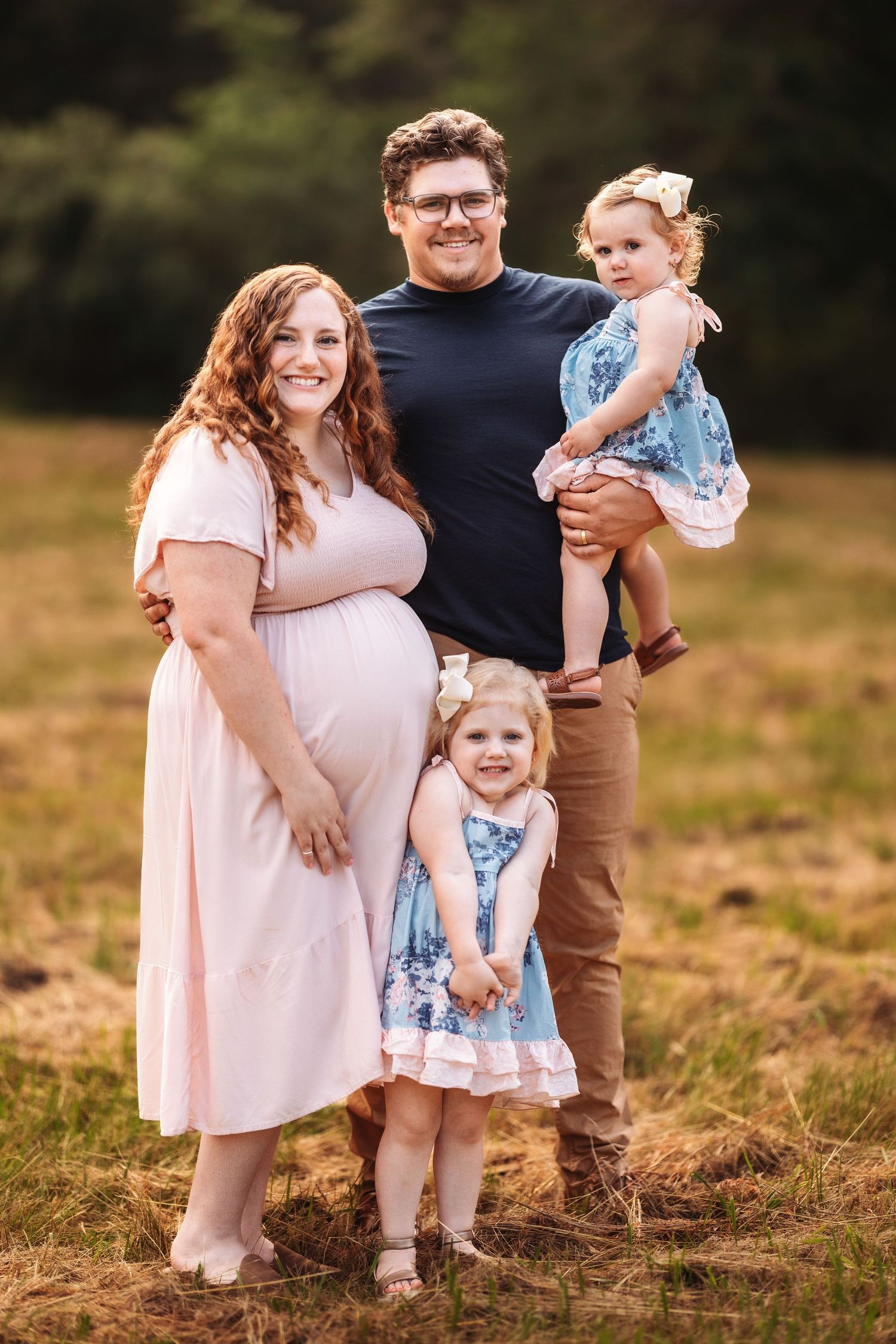 A family of four poses together outdoors in coordinated outfits with the children wearing matching blue dresses.