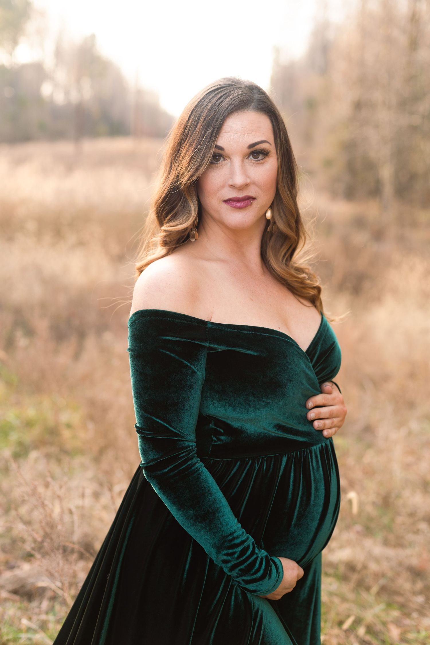 Maternity portrait of woman in off-shoulder emerald velvet gown in autumn field.