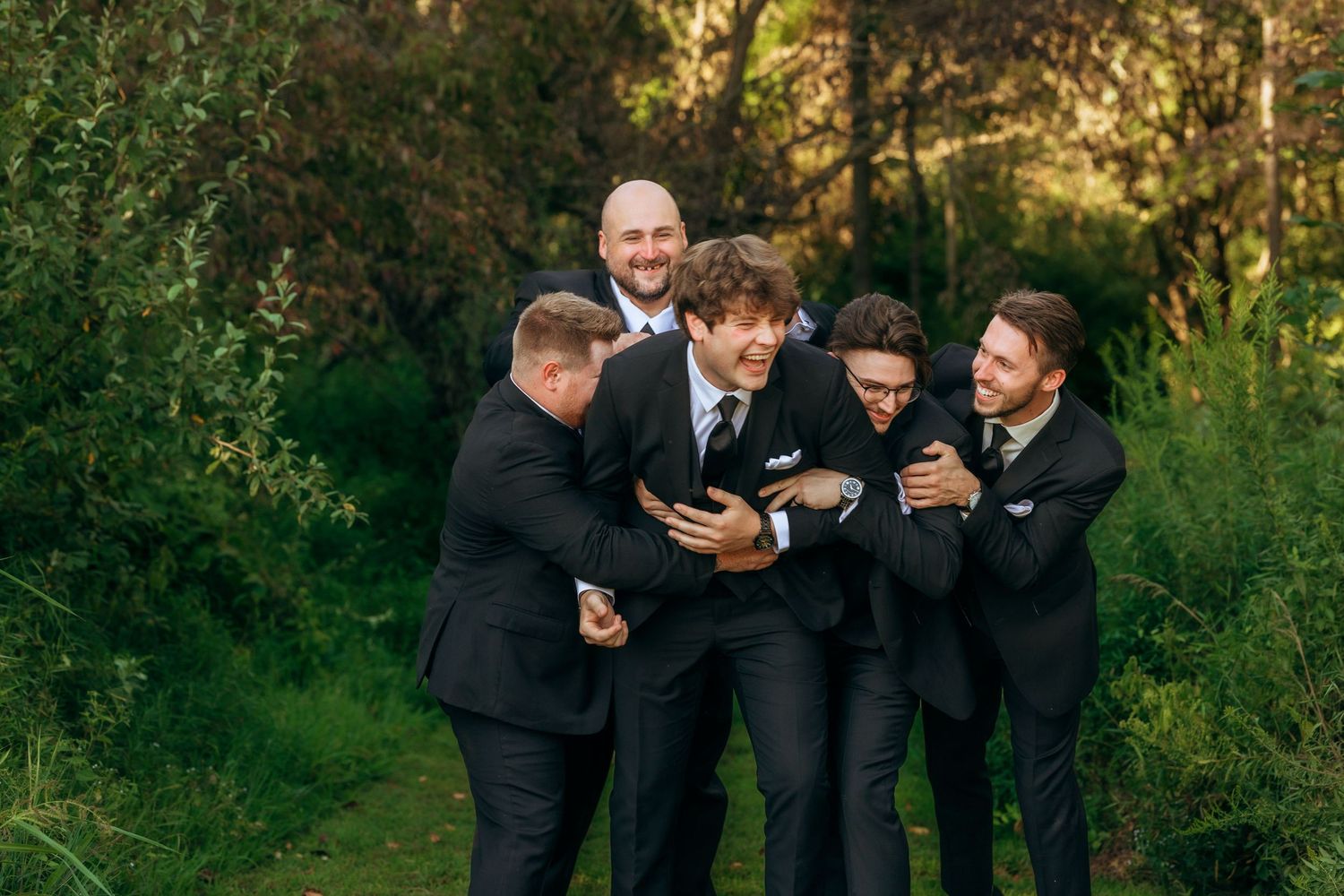 Group of groomsmen sharing laughs during outdoor wedding photo session.