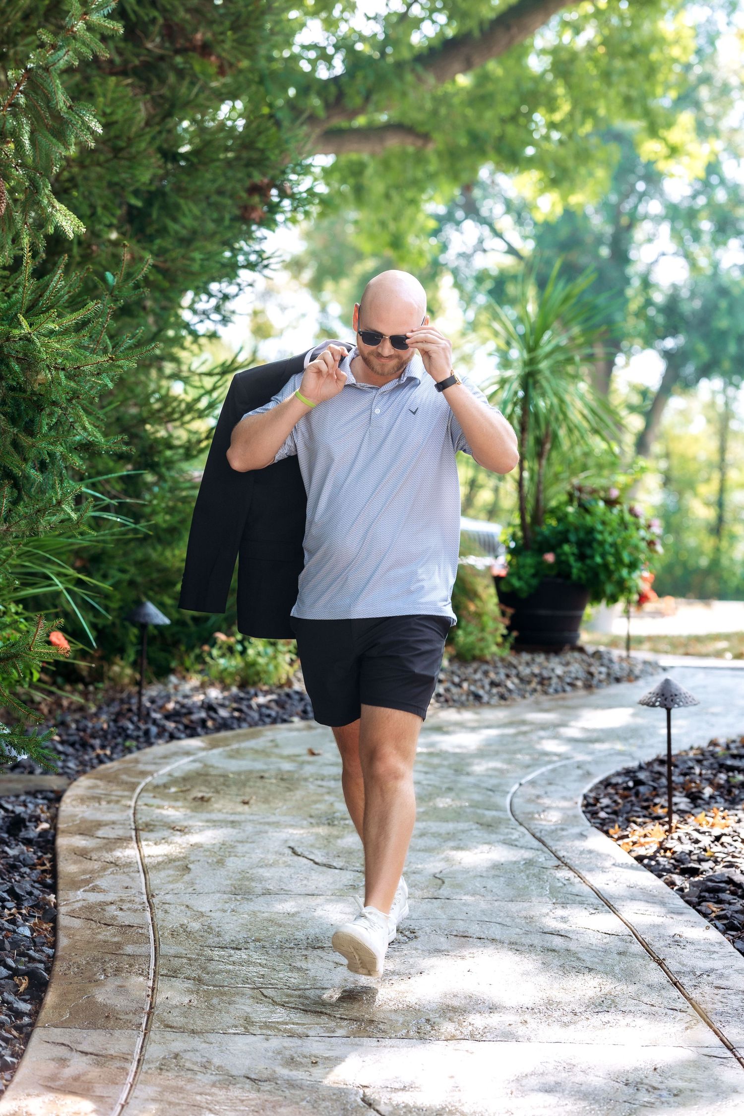 A man walking holding a suit over his shoulder outdoors on a winding garden path.