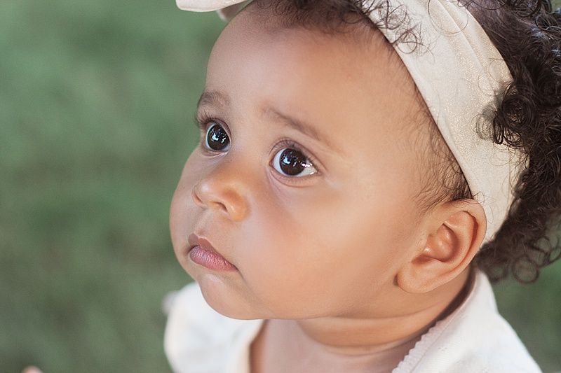 Close-up portrait of a beautiful baby with curly hair wearing a white headband.