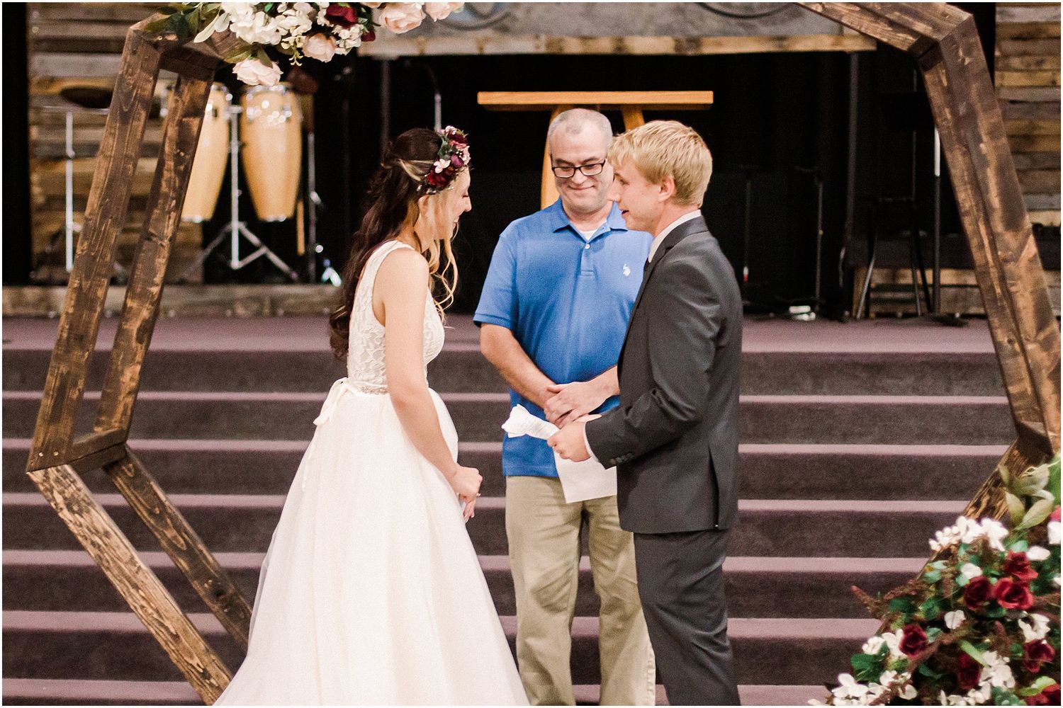 A wedding ceremony unfolds beneath a hexagonal wooden arch decorated with flowers and lanterns.