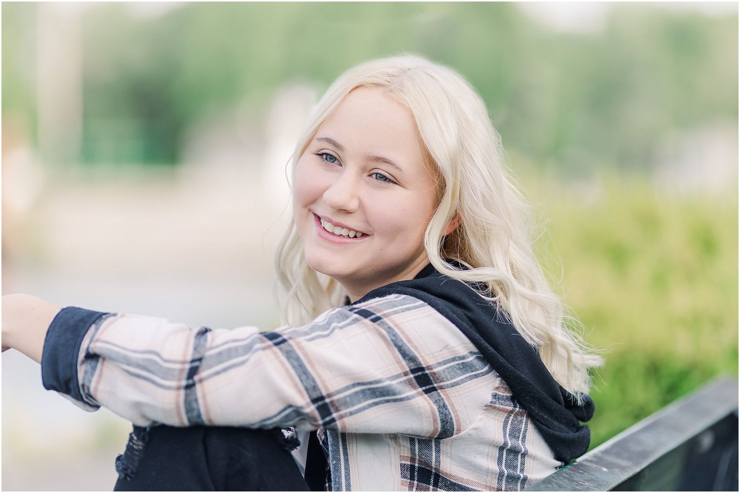 Senior girl laughs off camera while sitting on bench in between two boxwood shrubs