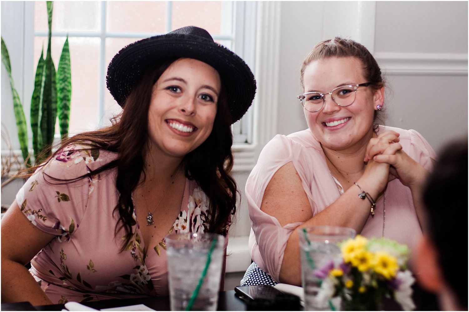 Two guests share a moment at a social gathering with yellow flowers on the table.