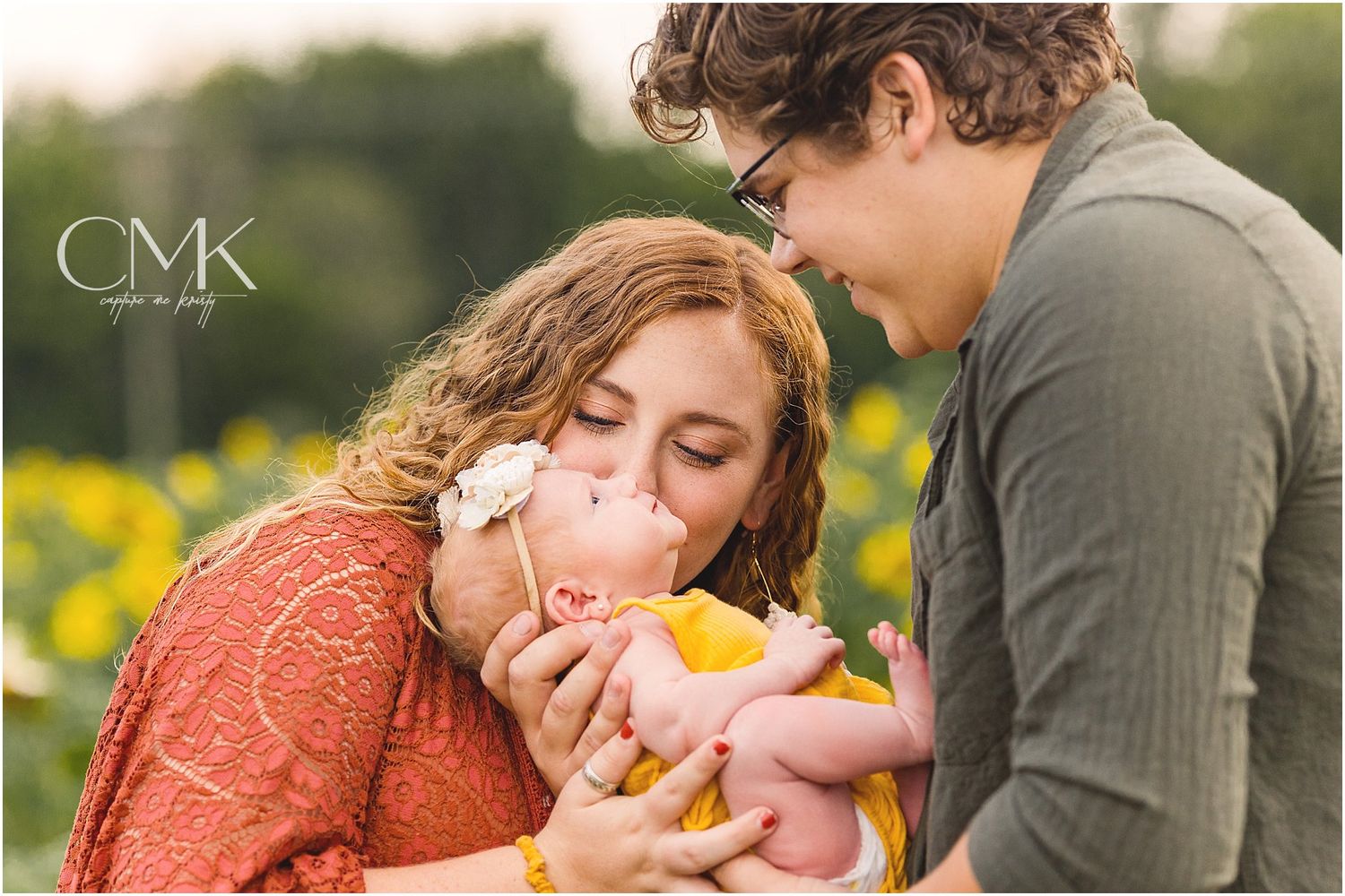 Intimate family moment with baby in yellow against field of wildflowers.