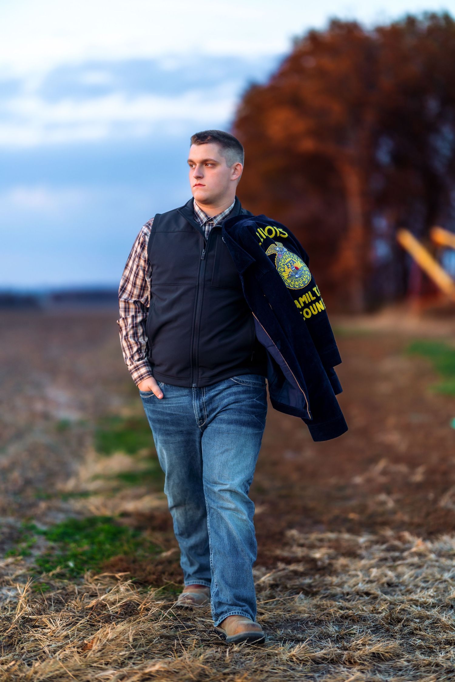 Rural portrait of person in FFA jacket walking along autumn field edge.