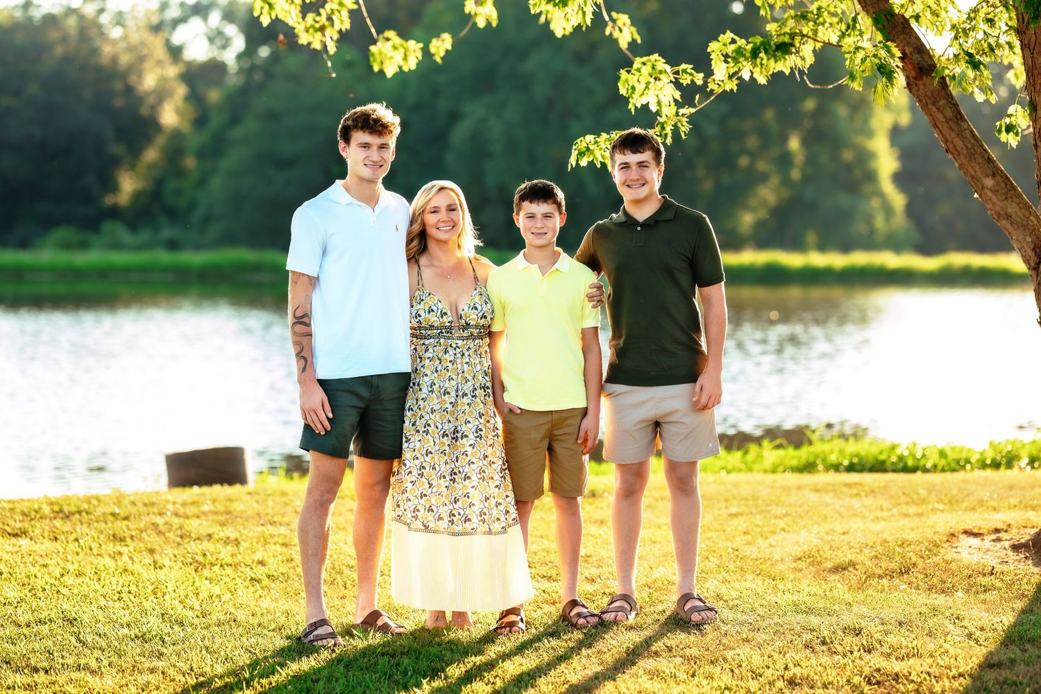 Family poses together by a lake during sunset with golden light filtering through trees.