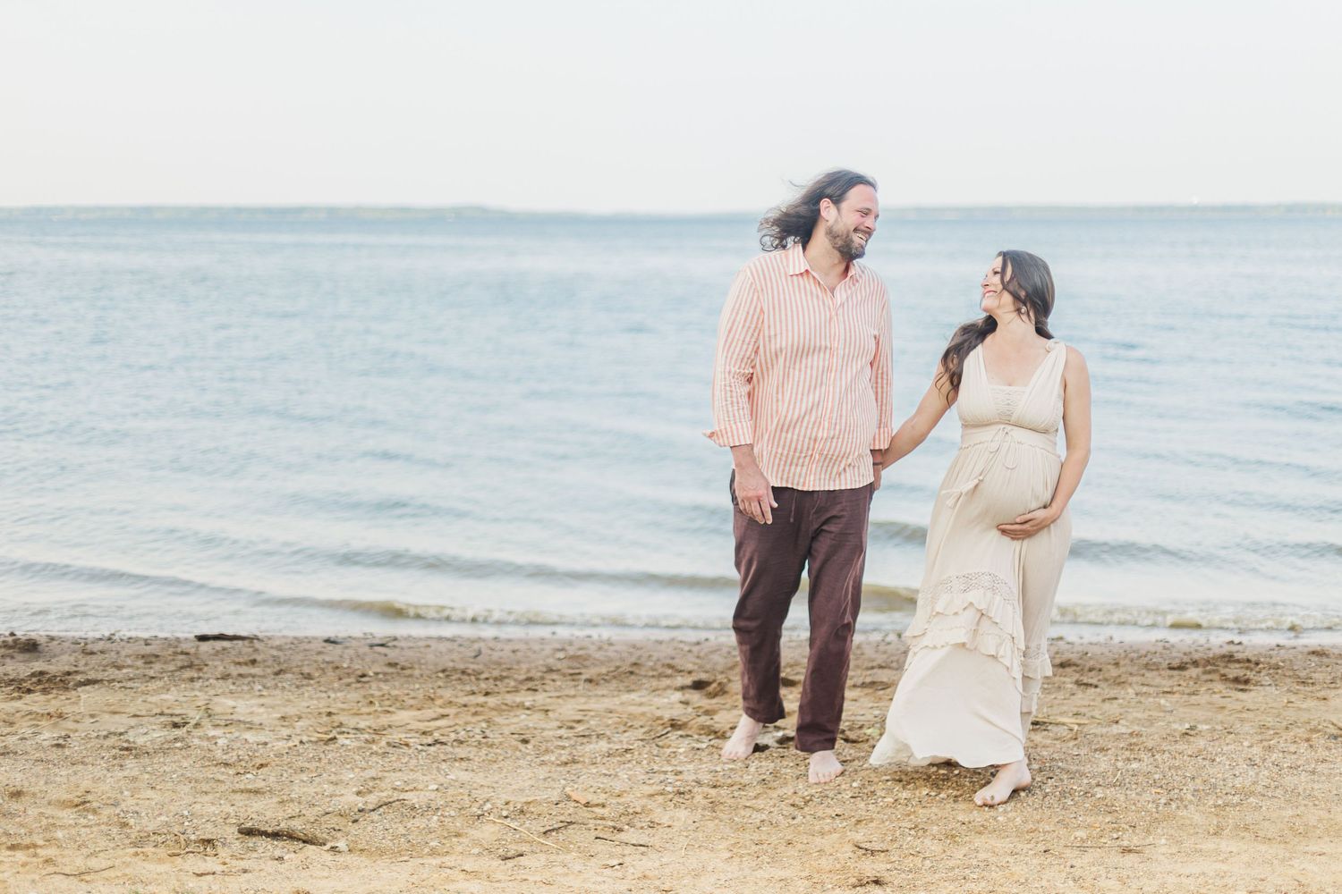 Couple walks along a serene beach shoreline at sunset.