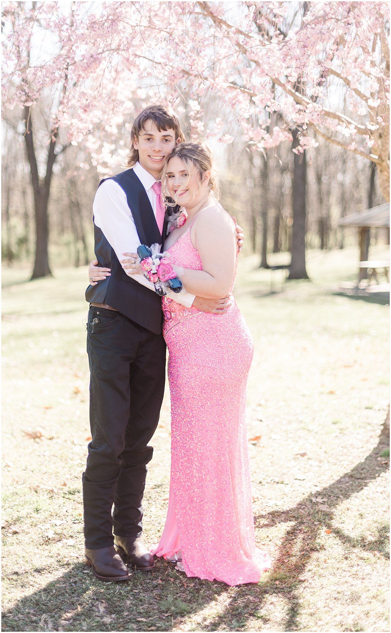 A couple shares an intimate moment in formal attire under blooming cherry blossom trees.