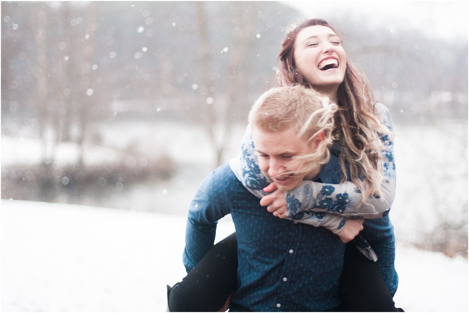 Joyful couple laughing during playful piggyback ride in snowy forest setting.