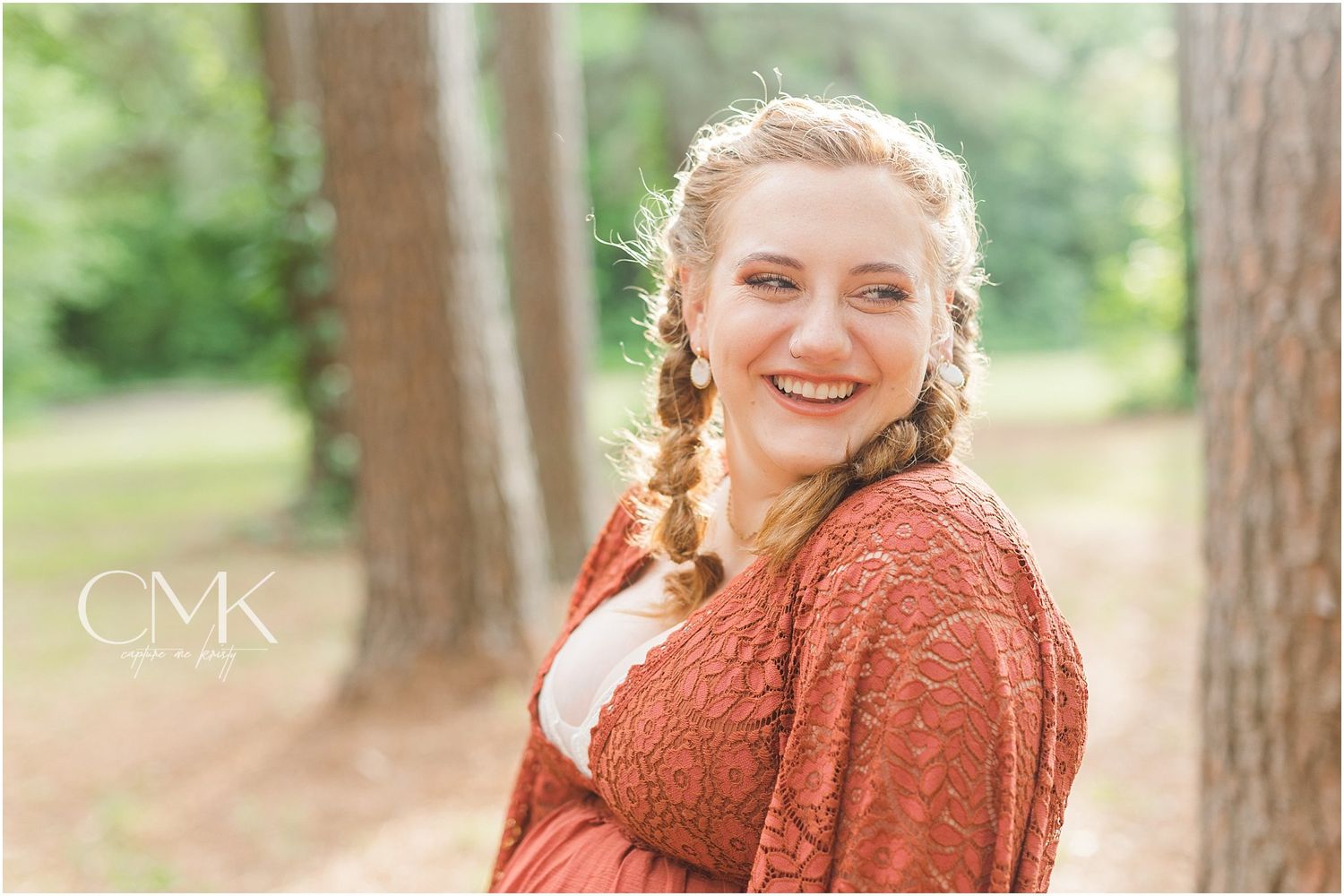 Radiant expectant mother with braided hair smiles during outdoor photo session.