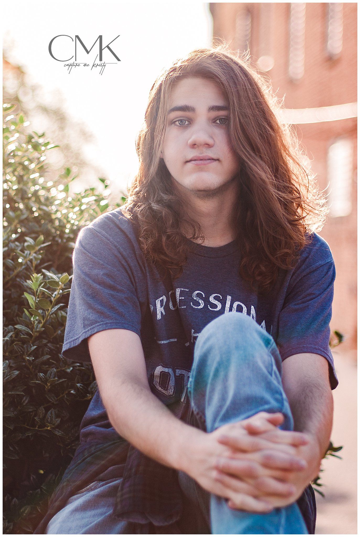 Person in navy t-shirt sitting outdoors against sunlit brick background.