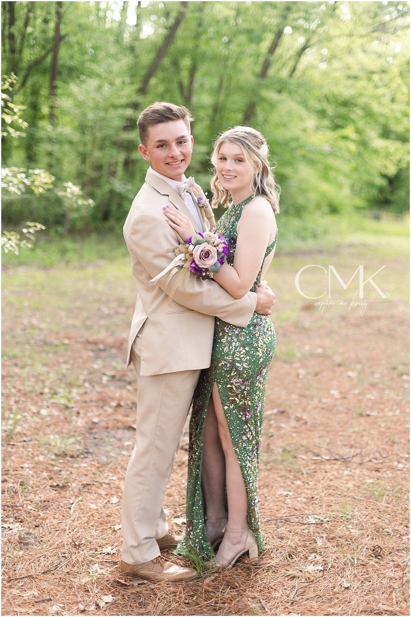 Formal portrait of a couple in the woods wearing tan suit and green sequined gown.