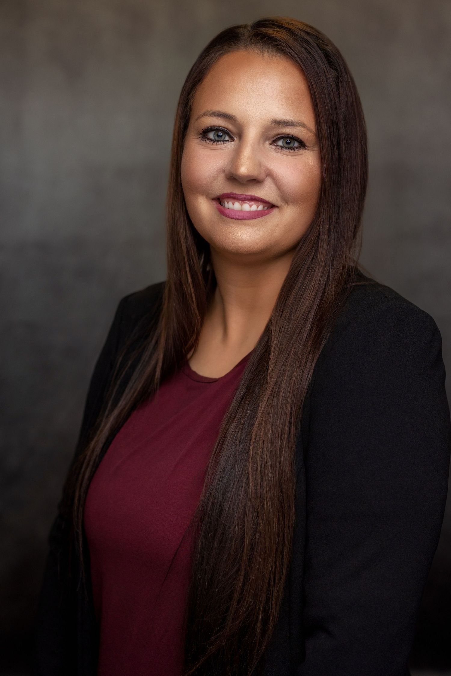 Studio portrait of woman with long dark hair wearing burgundy top and black blazer.