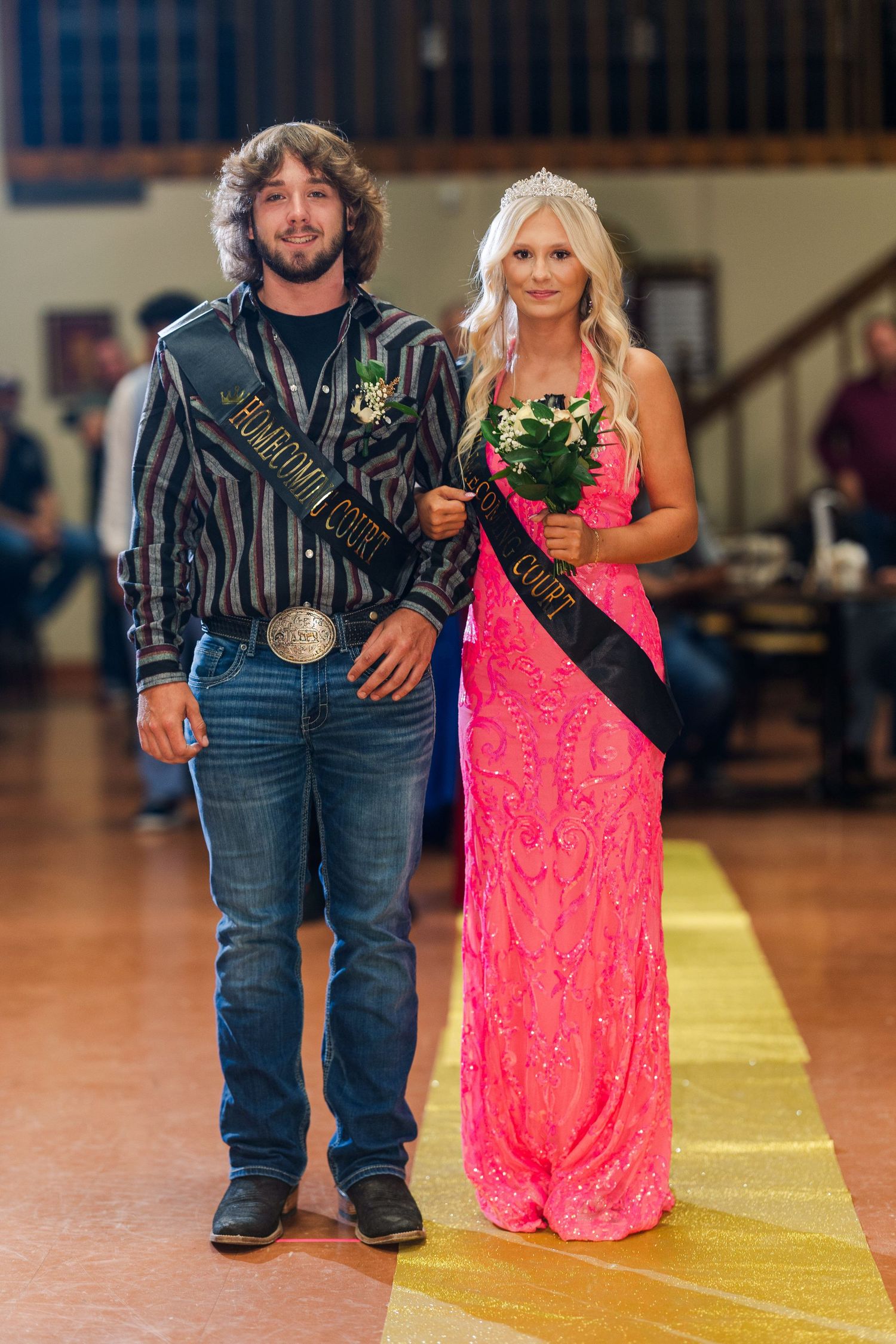 A couple in formal attire poses together on a yellow walkway at a special event.