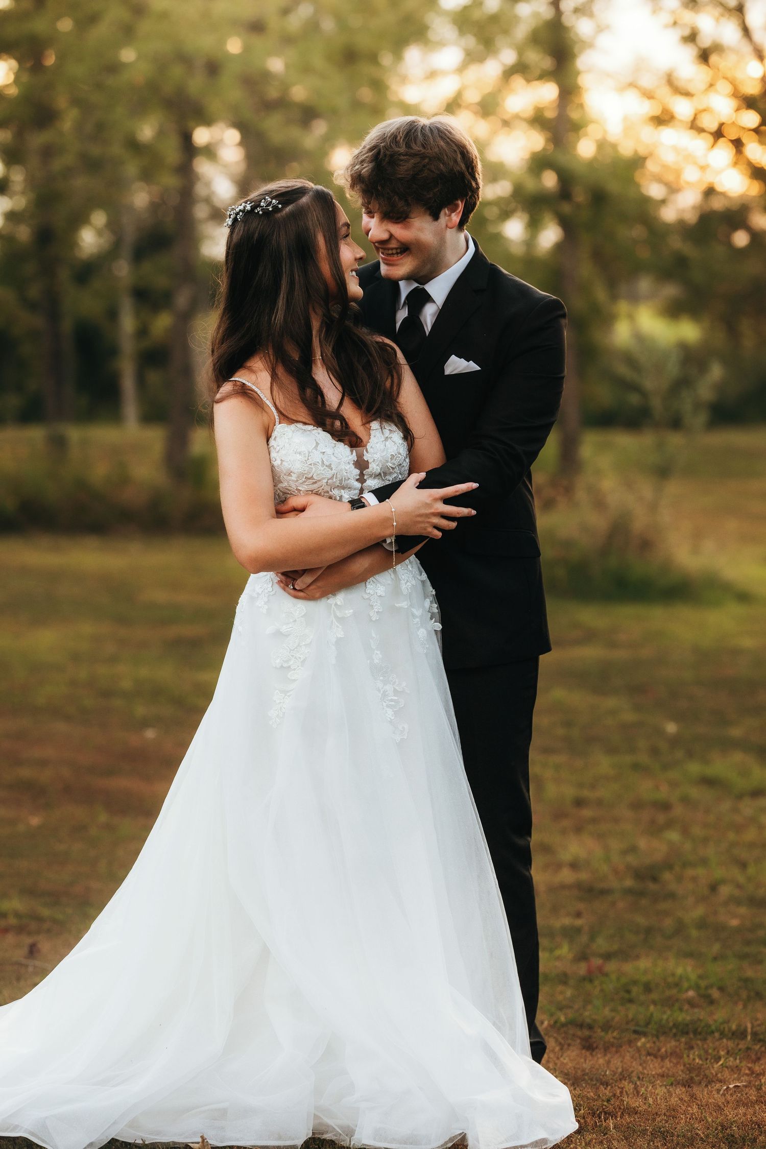 Romantic sunset wedding portrait with couple in formal attire embracing outdoors.