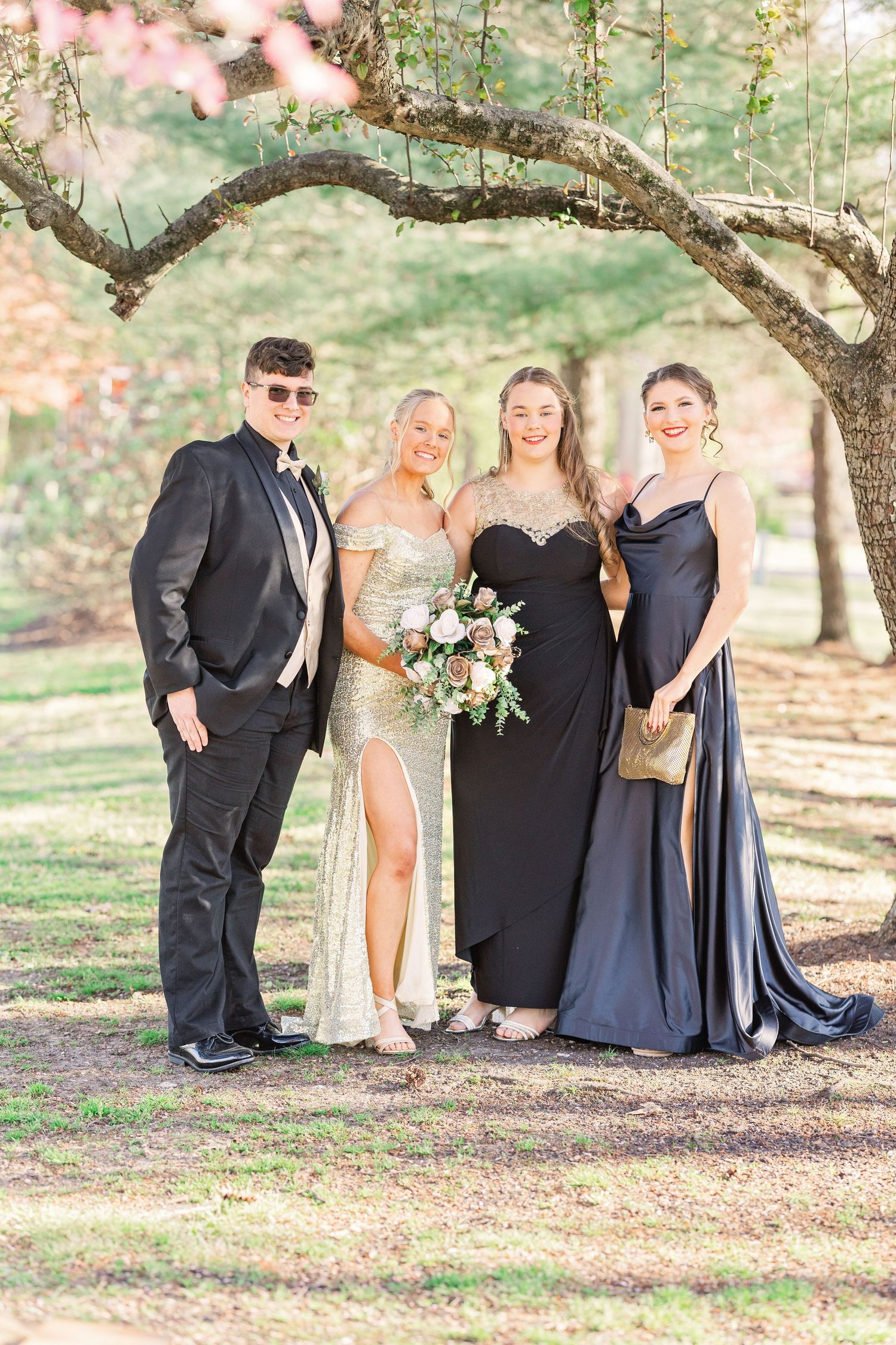 Group formal photo under blooming trees wearing coordinated evening attire.