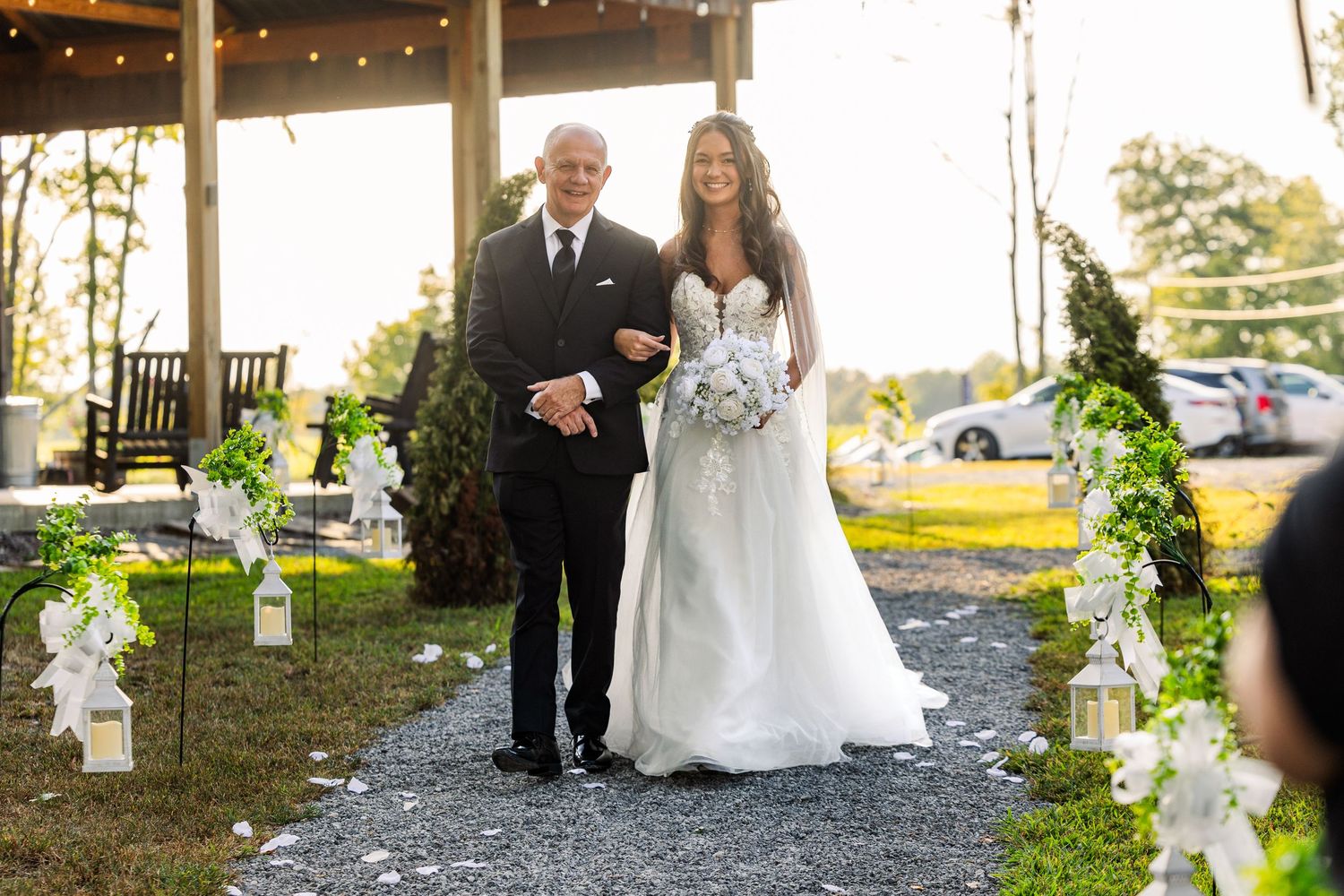 Wedding processional along decorated pathway with white floral arrangements and lanterns.
