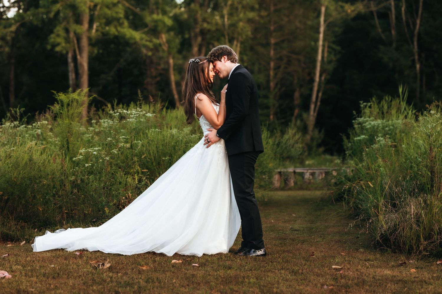 A wedding couple shares a romantic moment on a forest path surrounded by greenery.
