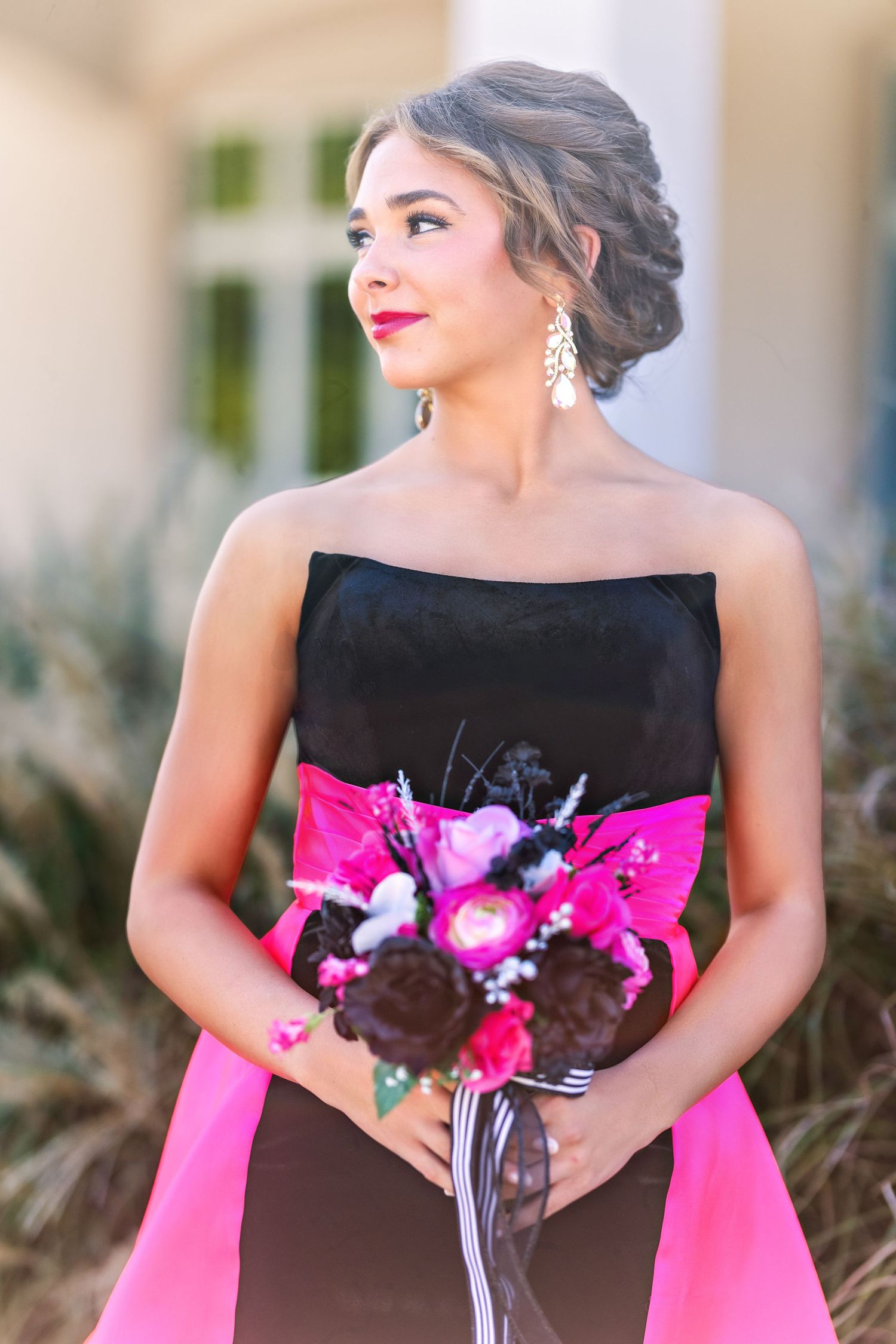 An elegant portrait showing a black and pink strapless gown with a bright floral bouquet.