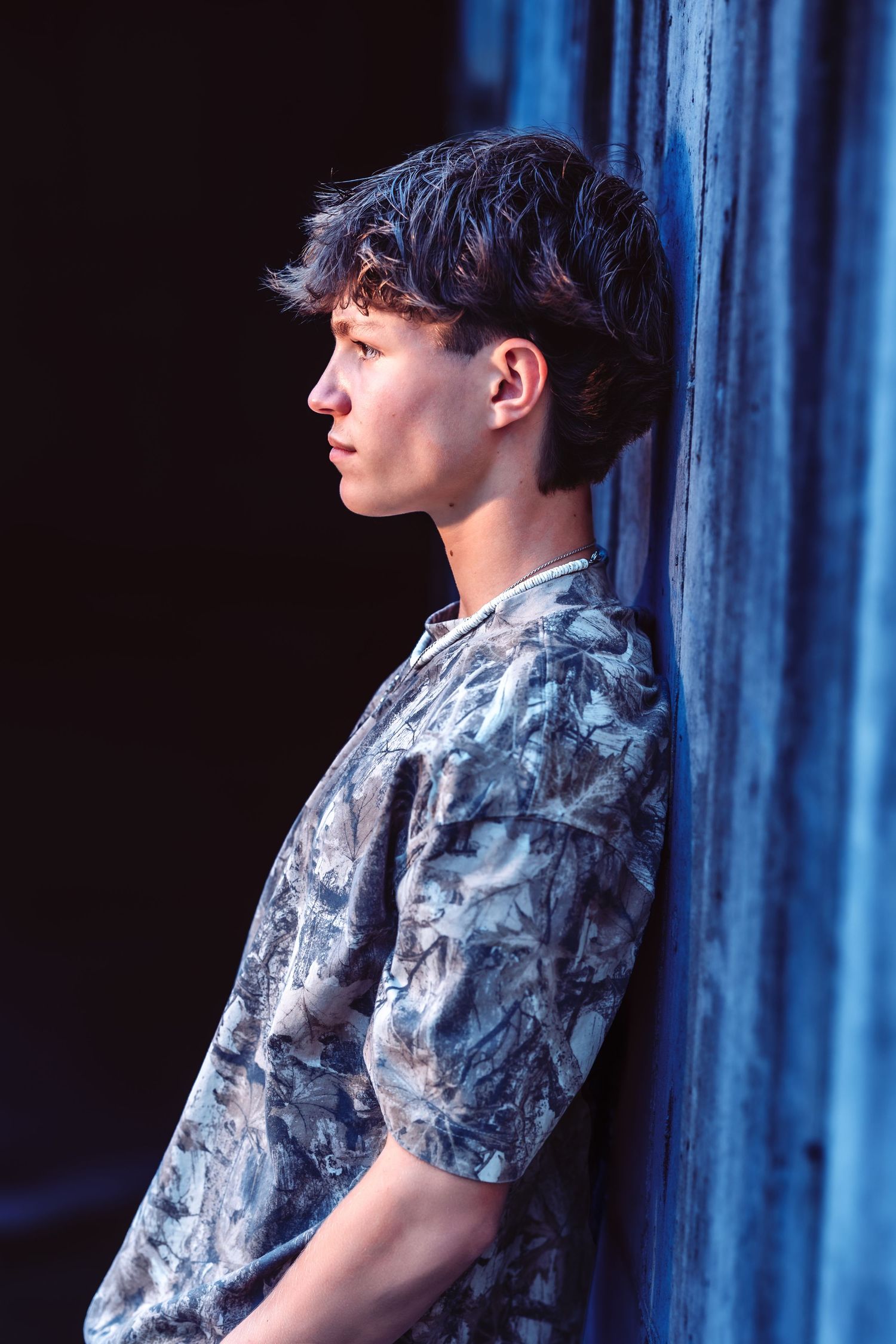 Person wearing a blue and white patterned short sleeve shirt poses against a dark blue curtain backdrop.