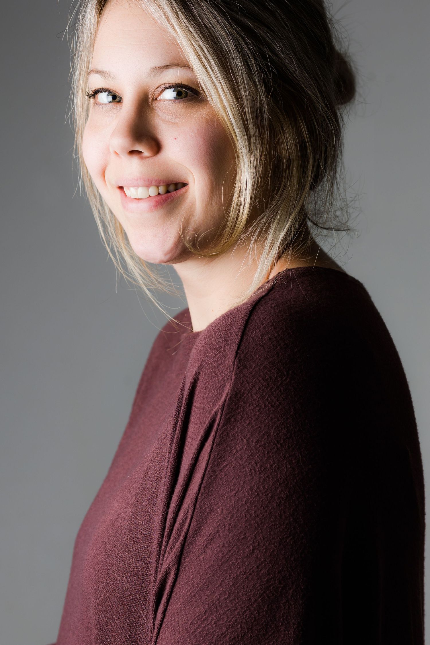 Professional portrait of a person in a burgundy sweater against a gray background.