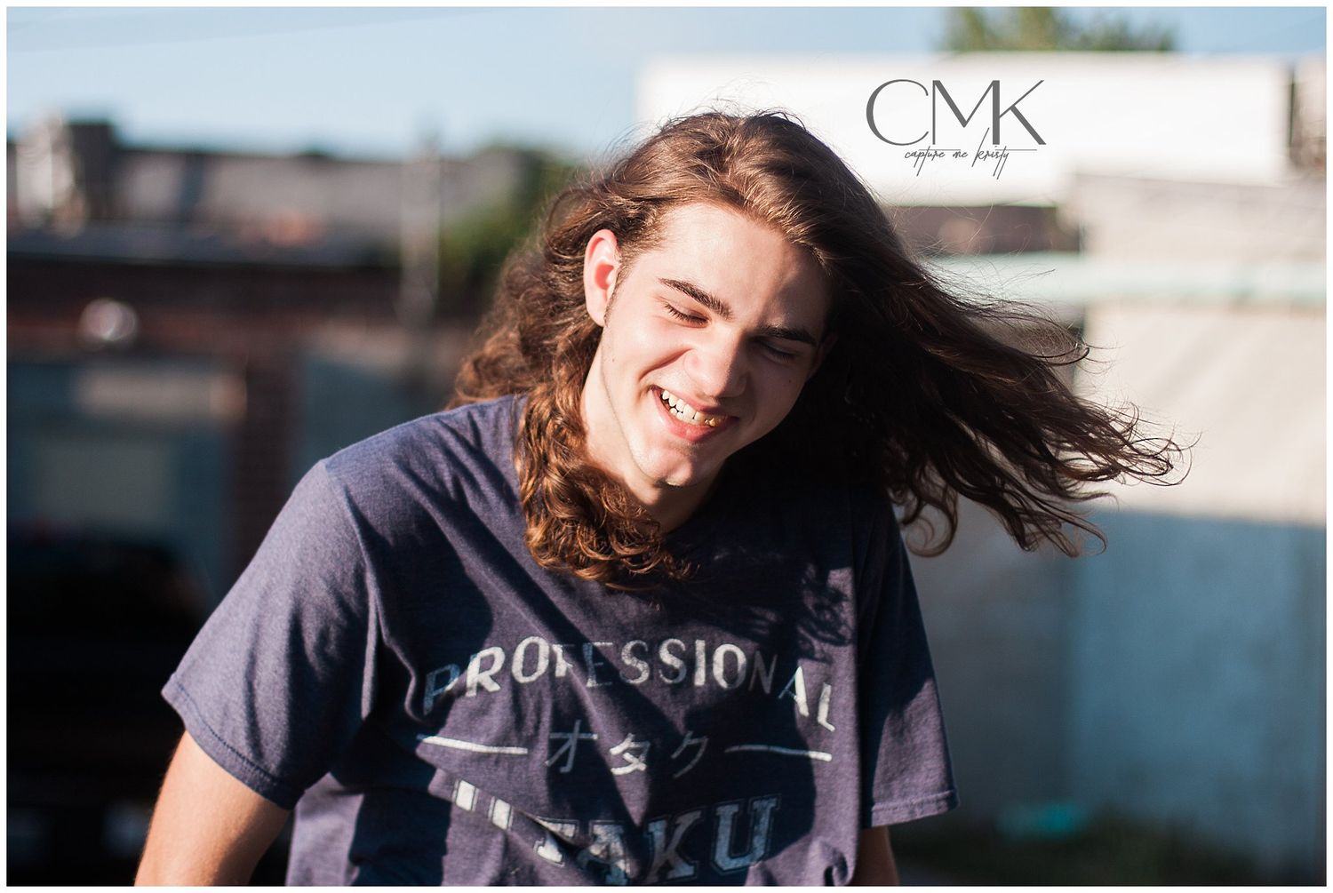 Person in dark t-shirt with flowing hair against outdoor backdrop.