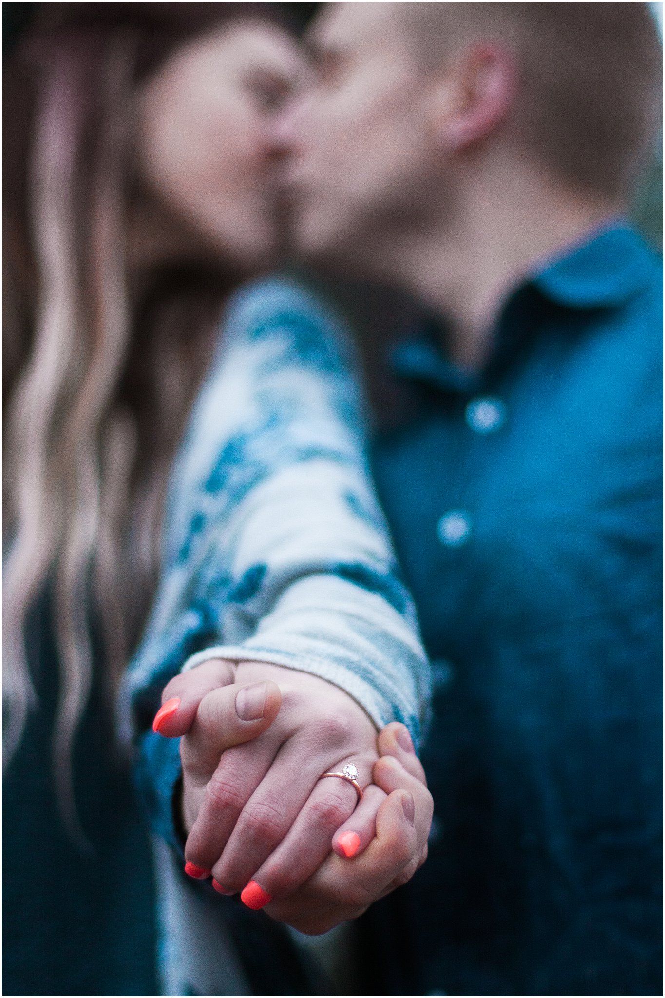 Close-up shot of couple holding hands with bright red nail polish against a blurred background.