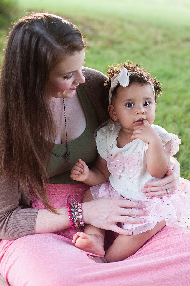 Sweet moment between parent and baby wearing a pink dress sitting outdoors.