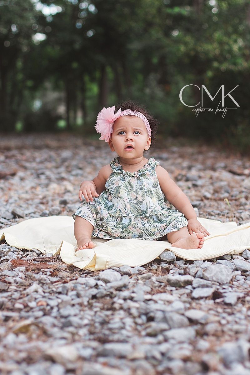 Baby in floral dress sitting on white blanket among rocks with CMK watermark.