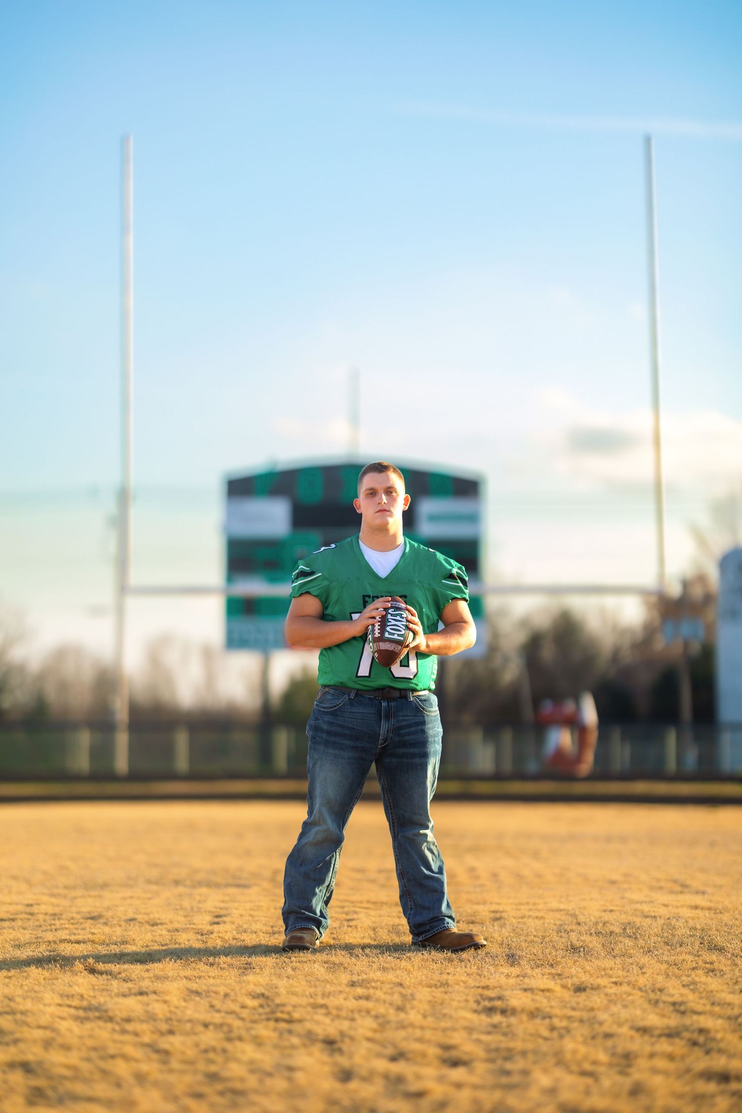 Football player in green jersey standing on field with goal posts in background.