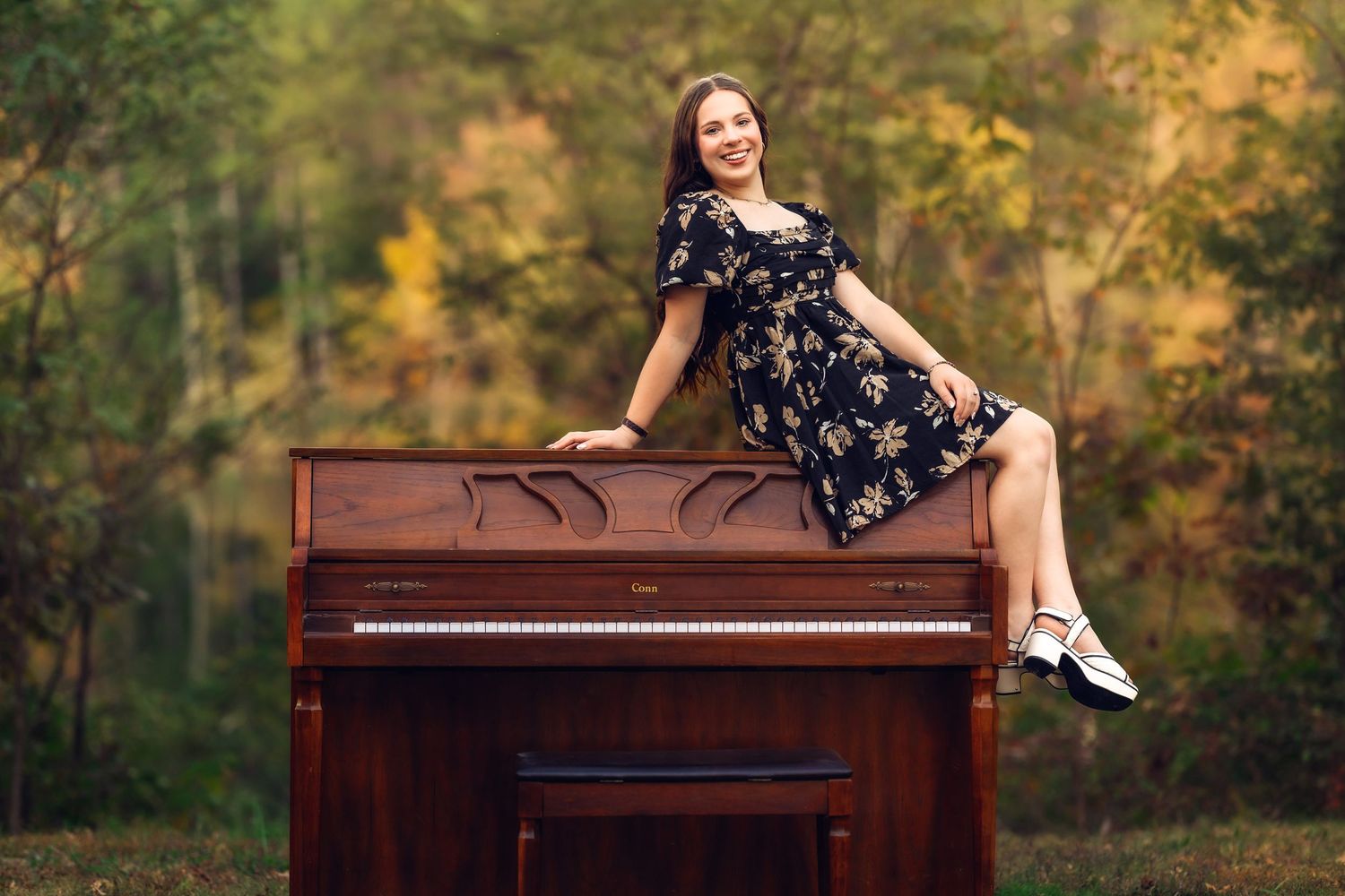 Figure in navy dress poses artistically on vintage piano outdoors during autumn season.