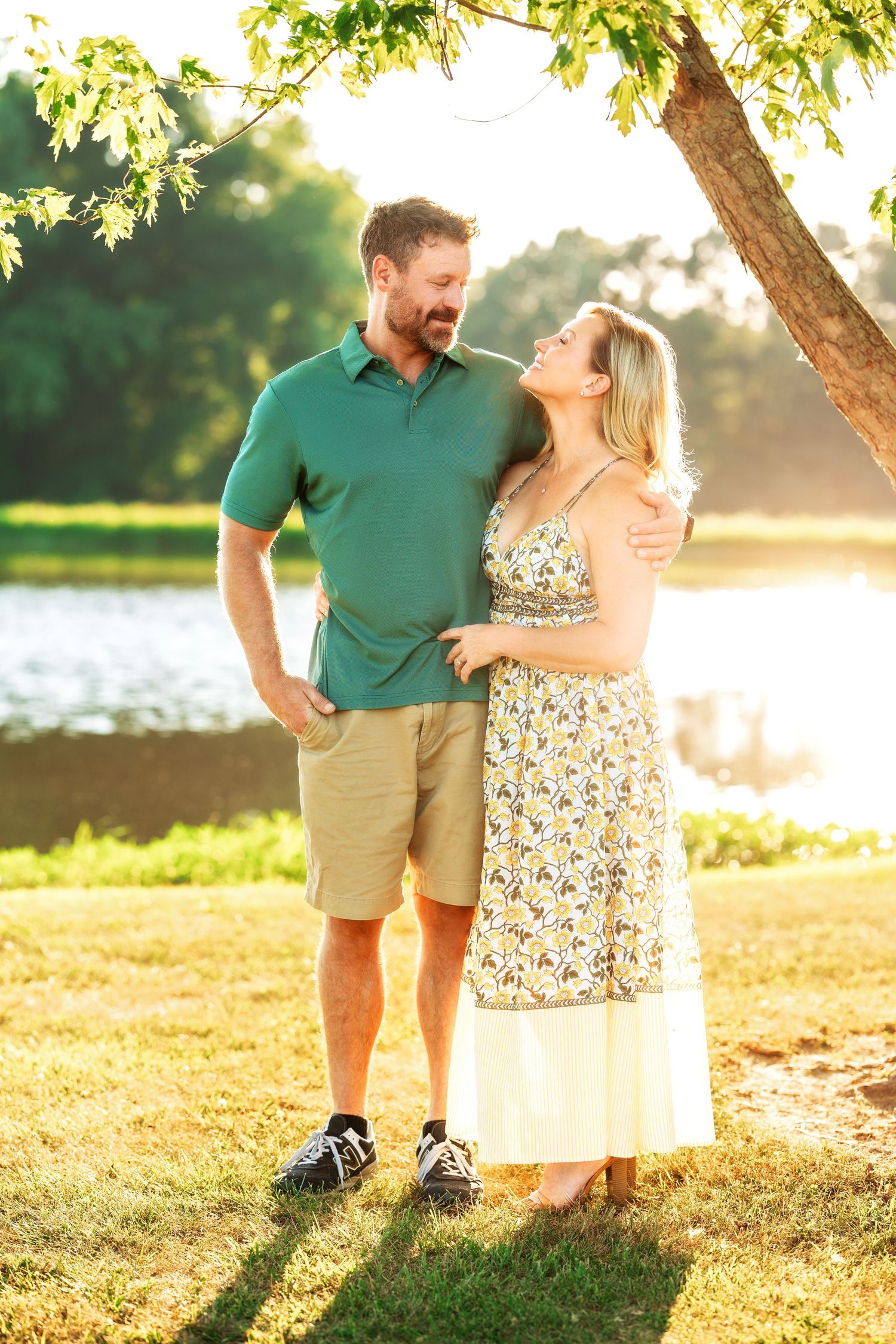 Couple poses together under tree branches with golden sunlight filtering through.