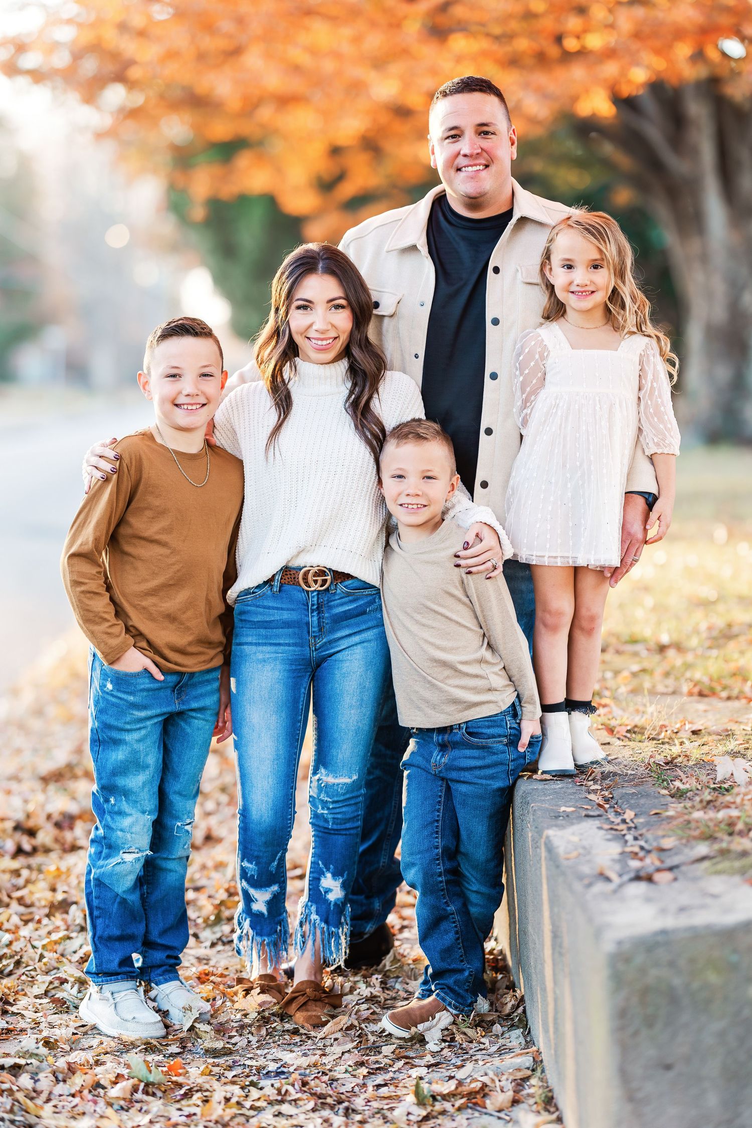 Family group poses together on autumn day among fallen leaves.