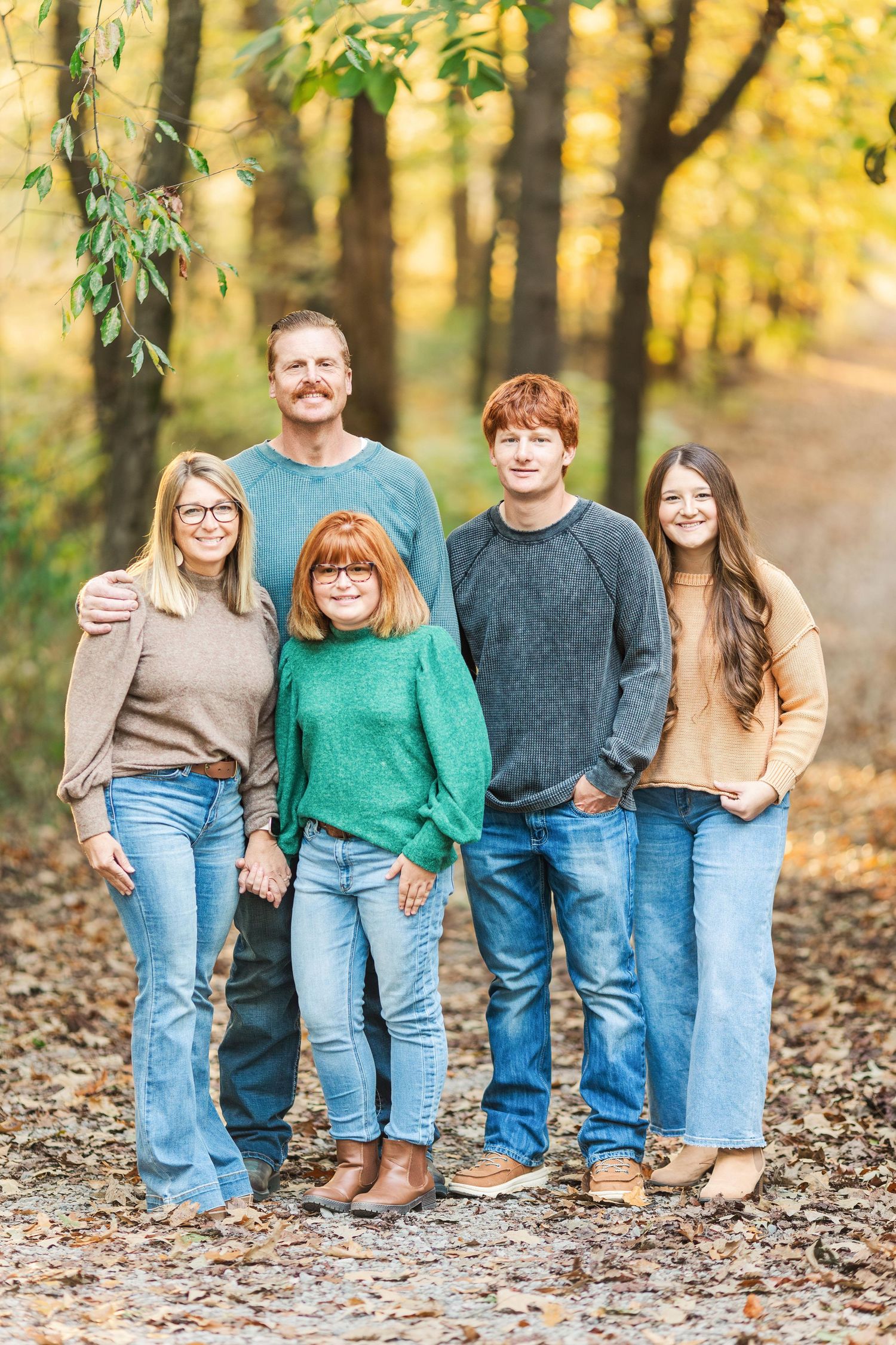 A family of five poses together on a leaf-covered path in coordinating fall sweaters.