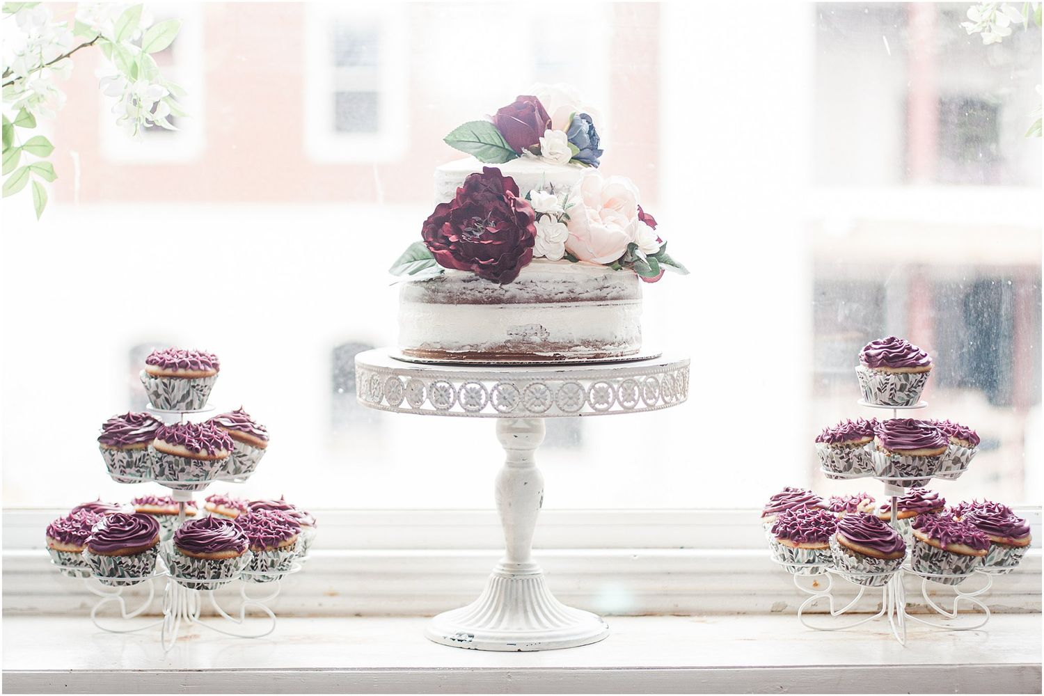 Minimalist wedding cake and cupcake display on white pedestal stands.