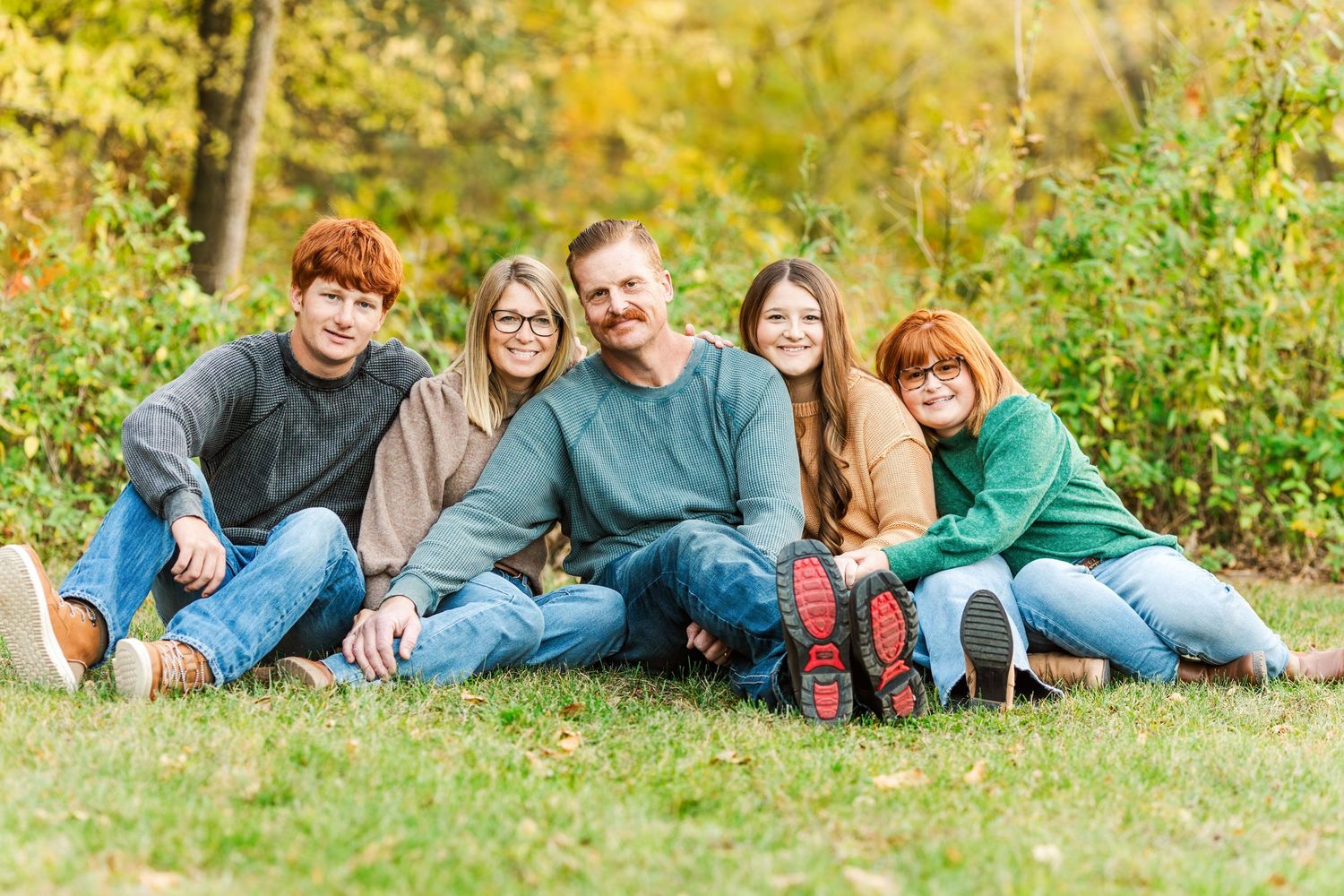A family group relaxes together on green grass during fall.