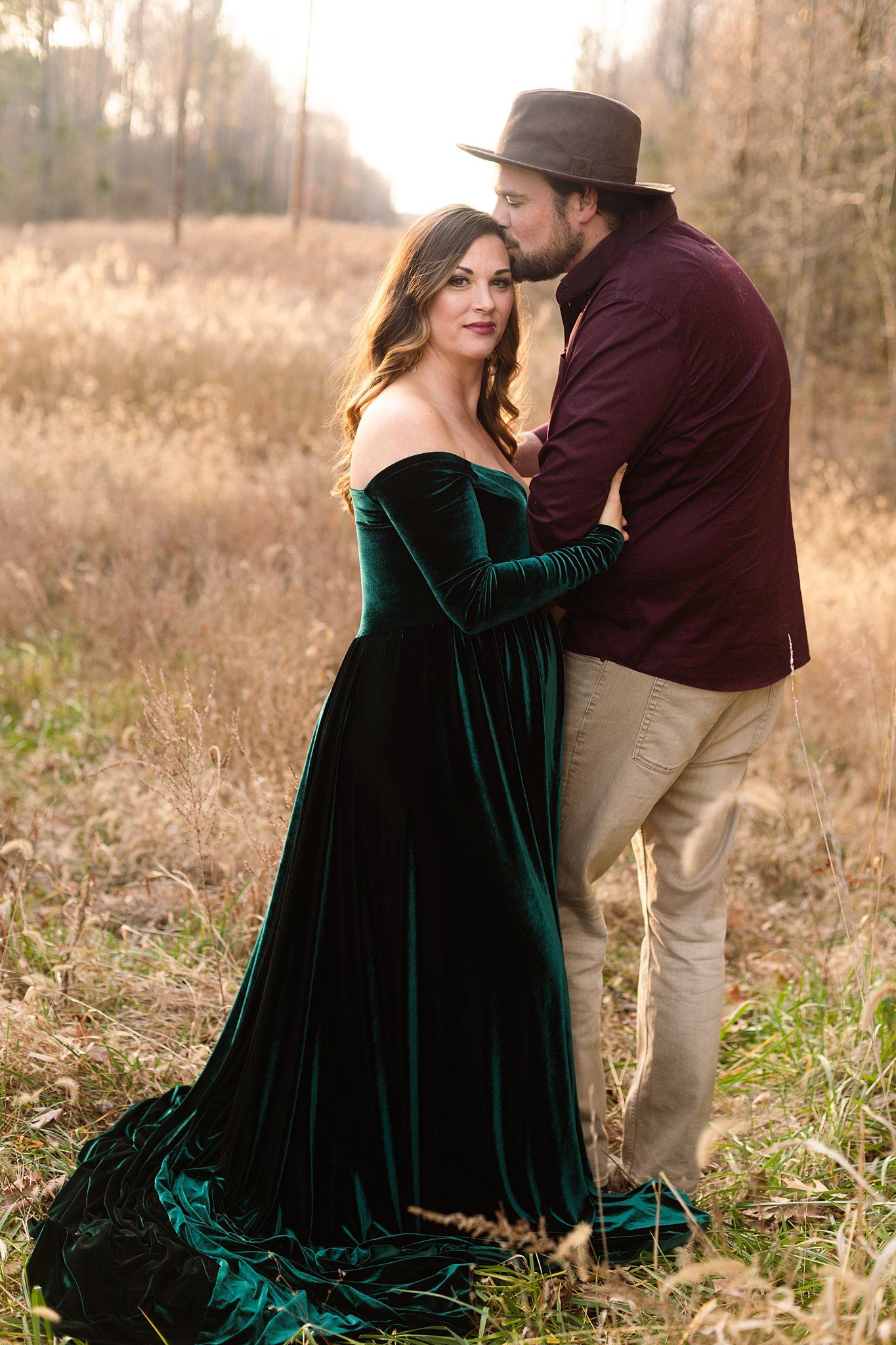 Sunset maternity photo featuring emerald velvet dress against autumn field backdrop.