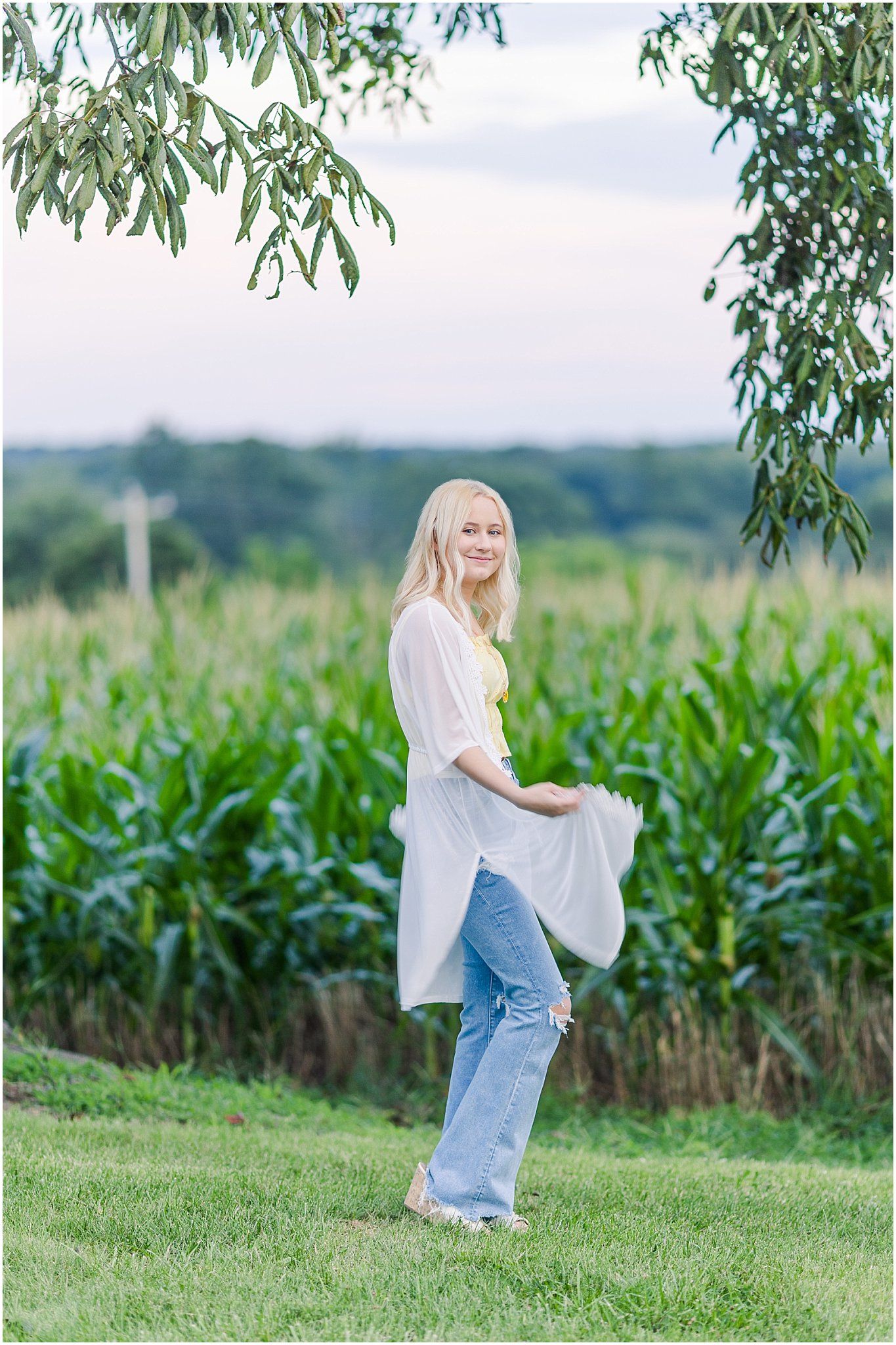 senior girl twirling robe in front of corn field at sunset