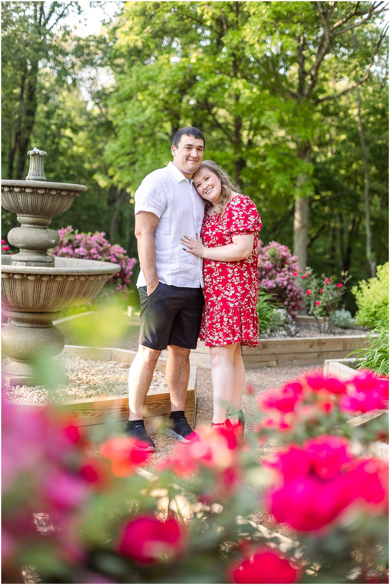 Couple standing by tiered fountain with vibrant pink flowers in foreground.