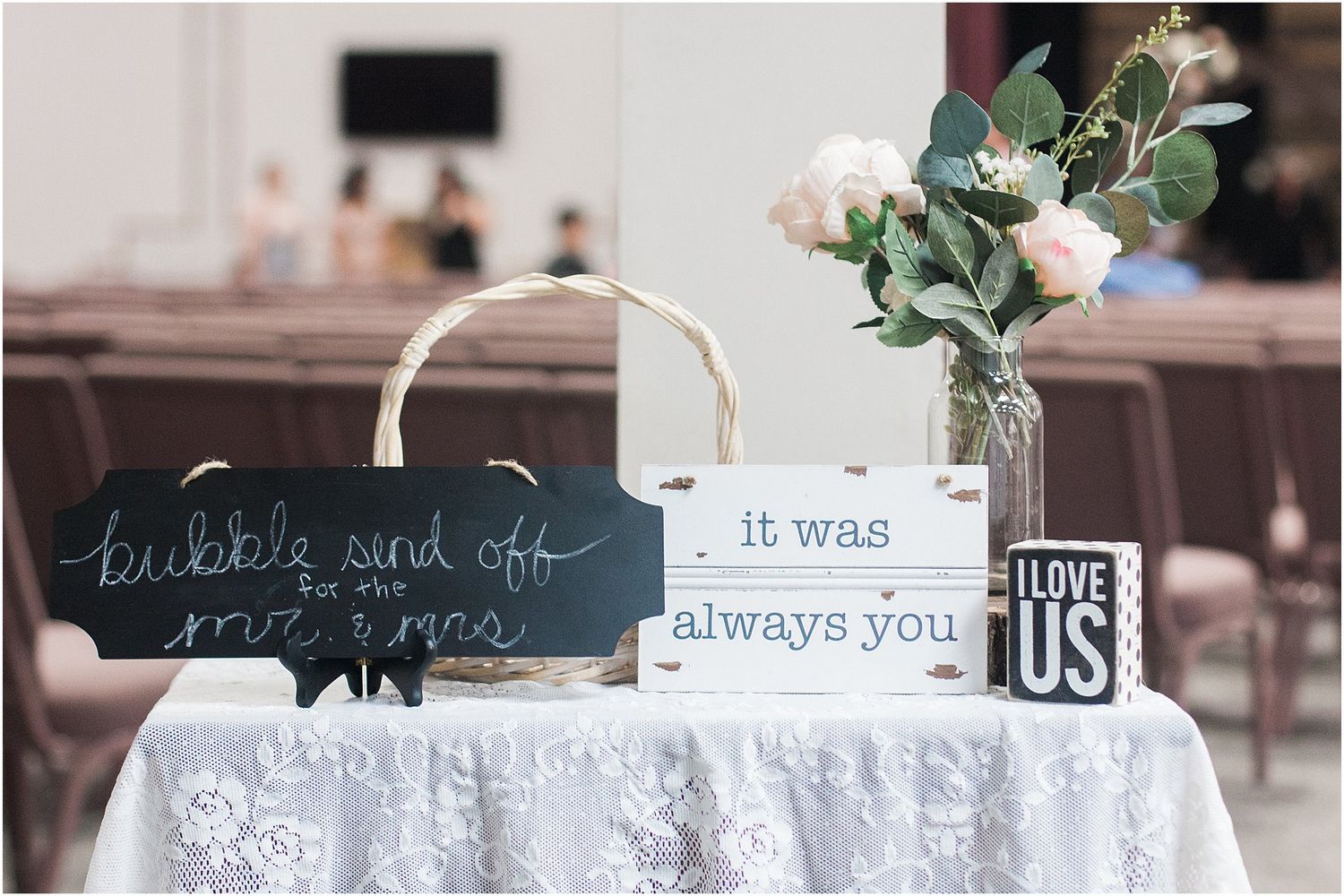 Wedding decor featuring signs and vase on white lace tablecloth with romantic messages.