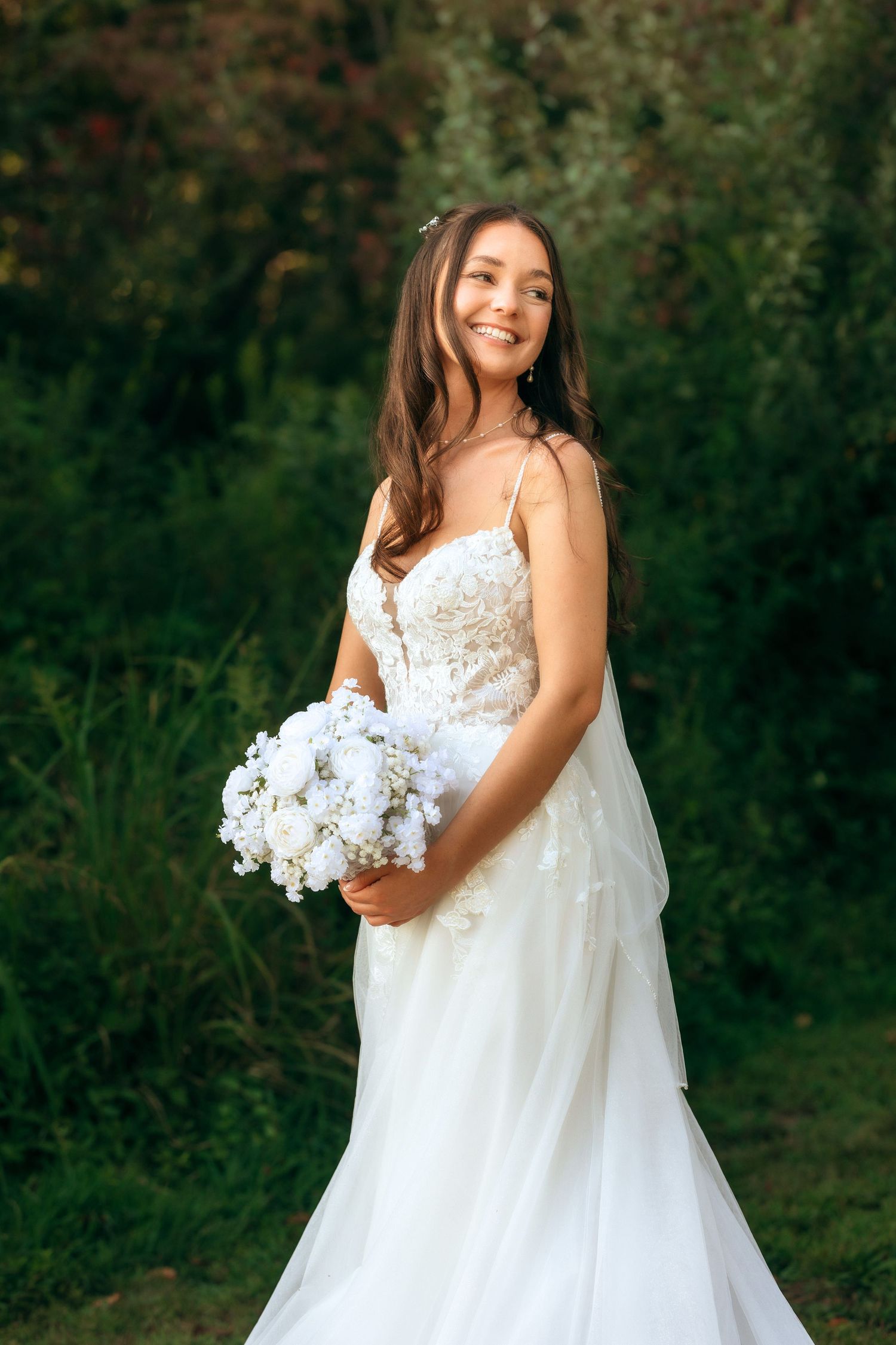 Ethereal bridal portraits in white lace gown holding white bouquet against dark background.