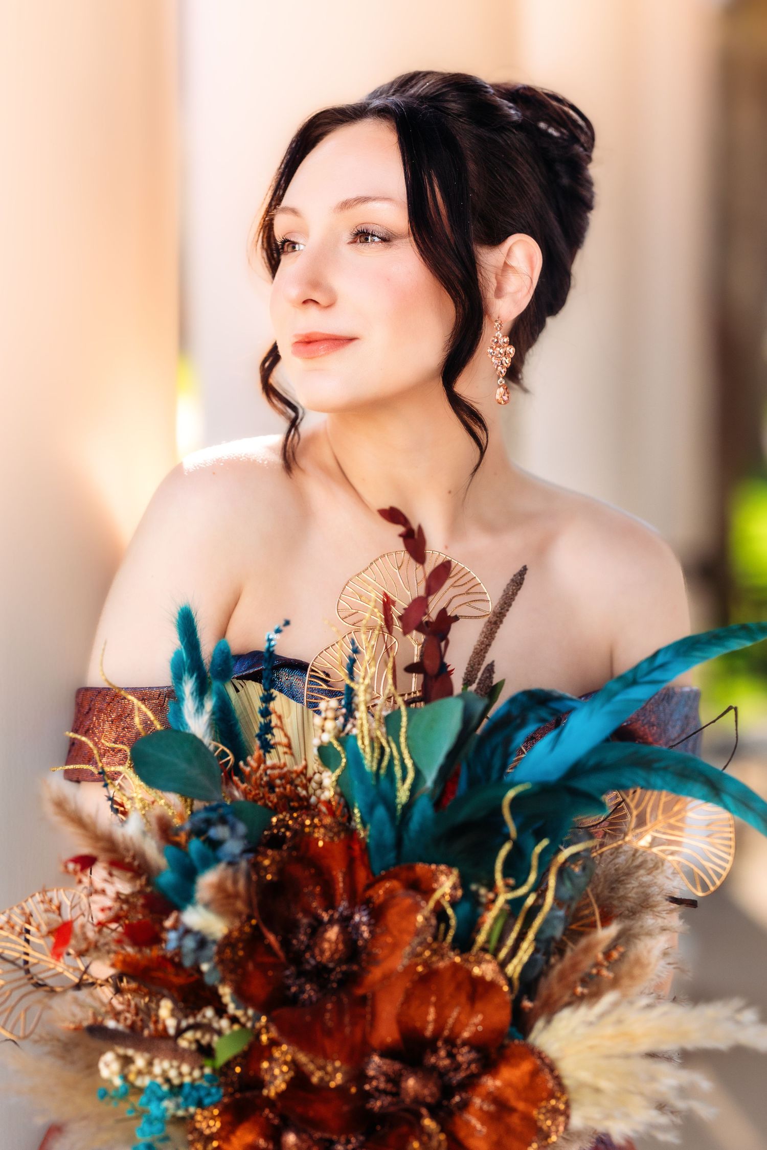 Elegant bridal portrait with a vibrant dried floral bouquet featuring teal and rust-colored blooms against a warm background.