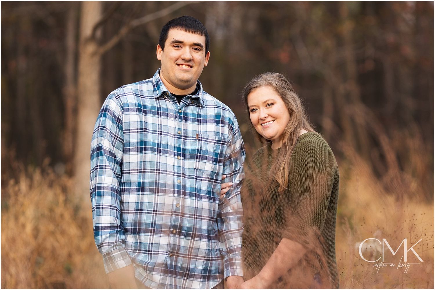Natural light portrait of couple in coordinated casual outfits against wooded backdrop.