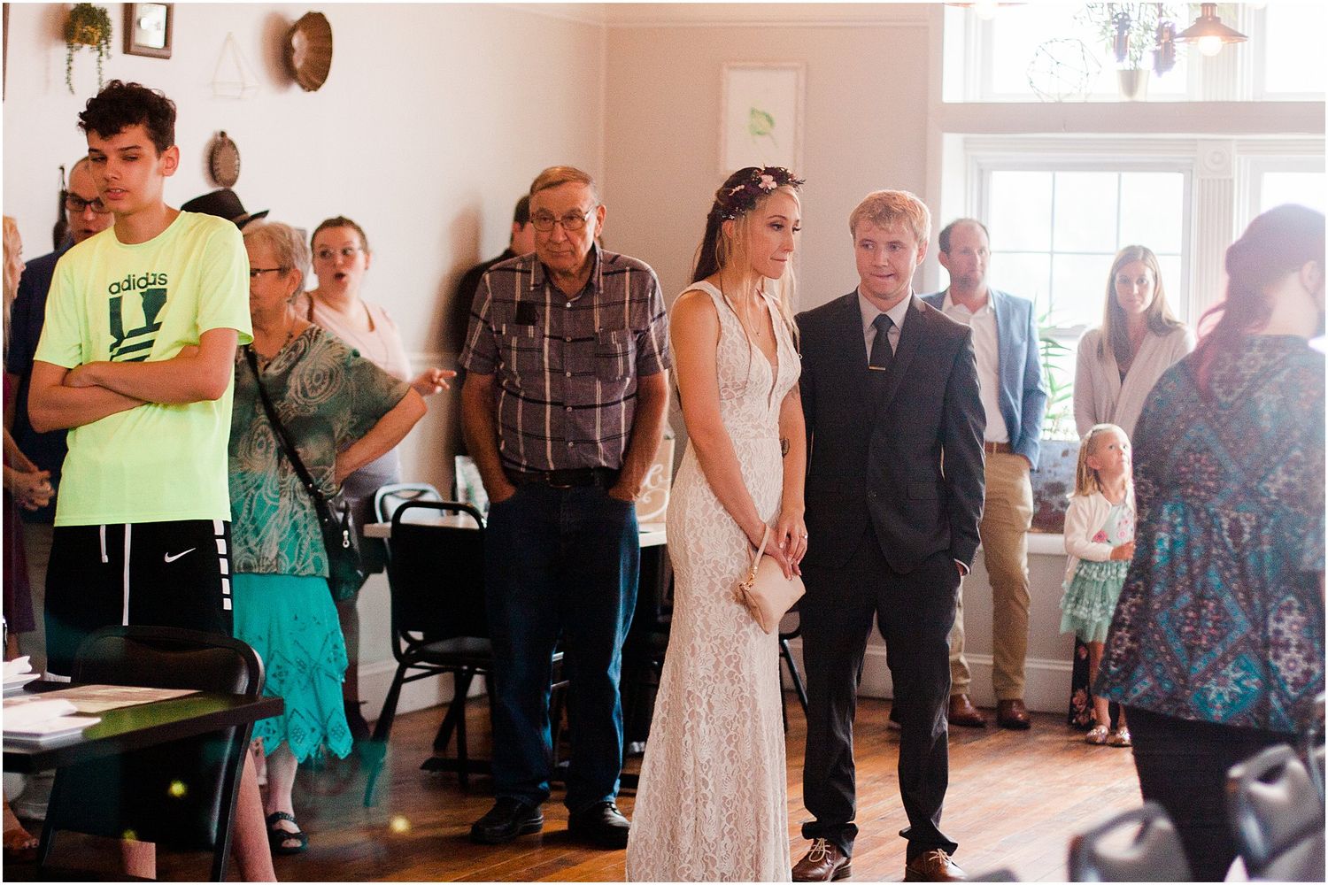 Wedding guests stand in a bright indoor venue during a ceremony.